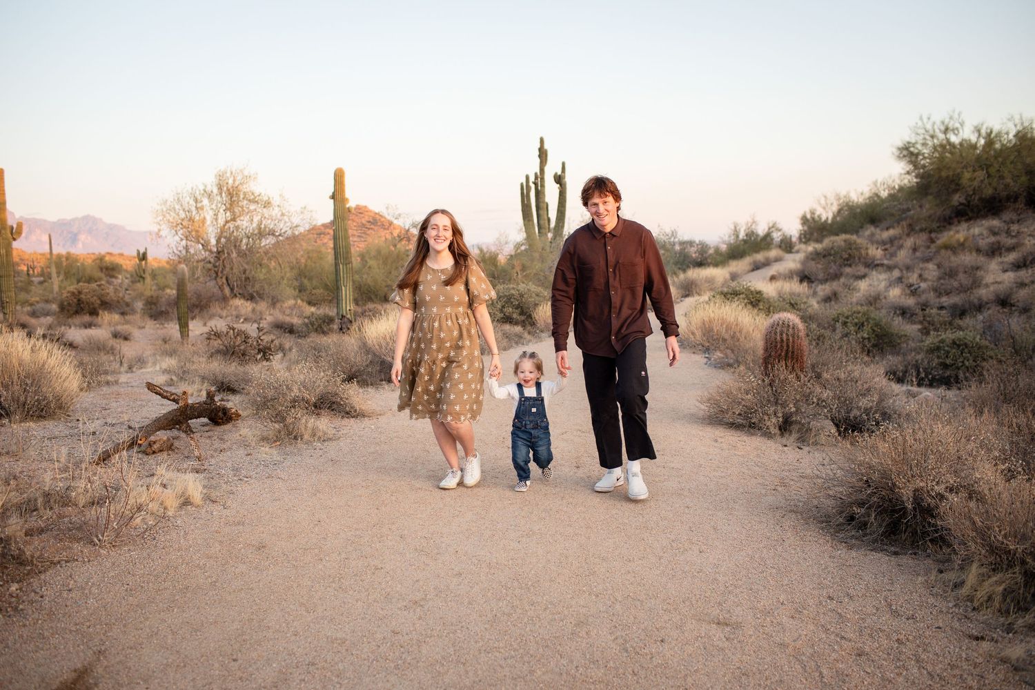 Desert landscape photoshoot at sunset with people walking along a sandy path.