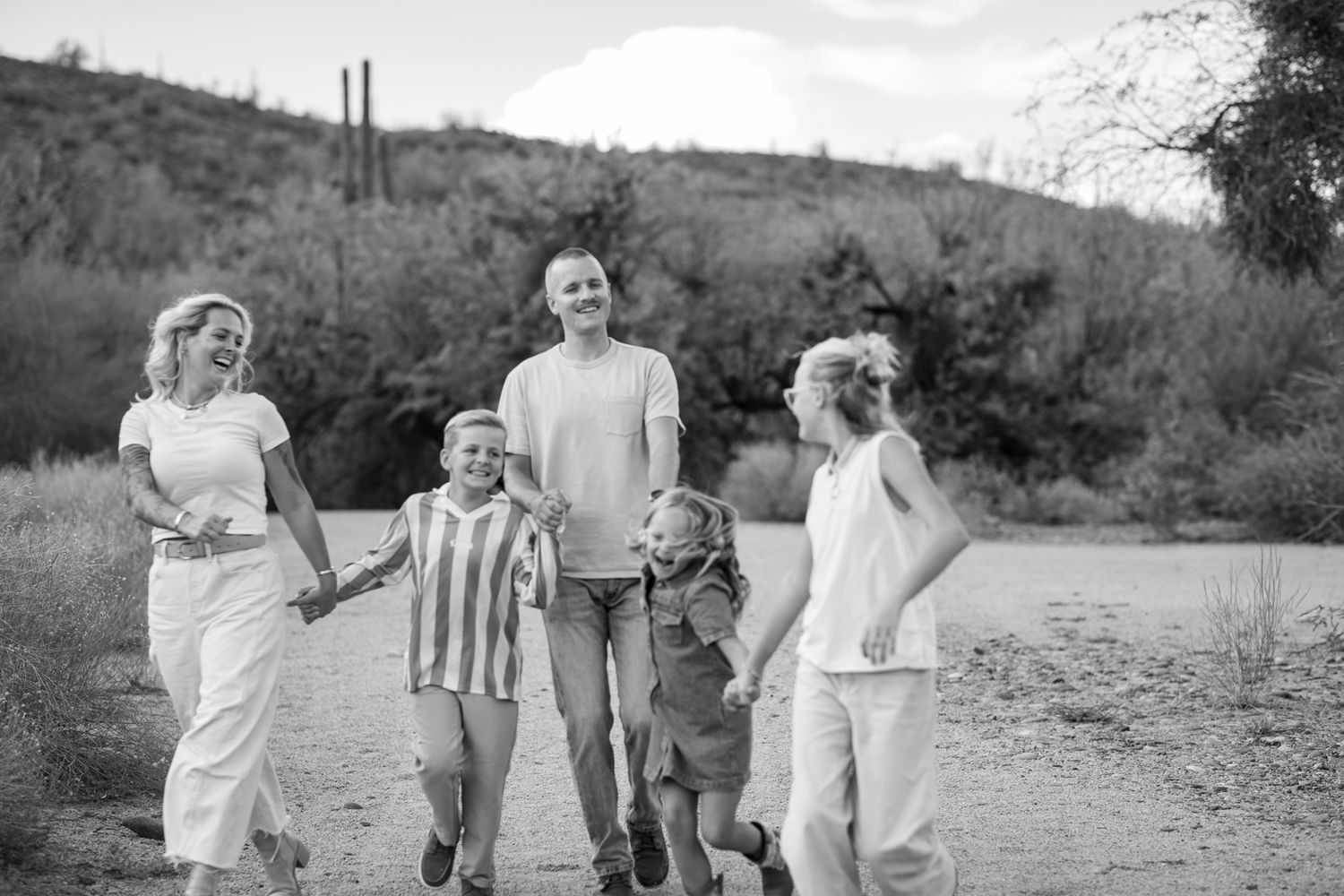 A group in white and striped outfits runs playfully along a dirt path in a natural outdoor setting at Water Users recreational area.