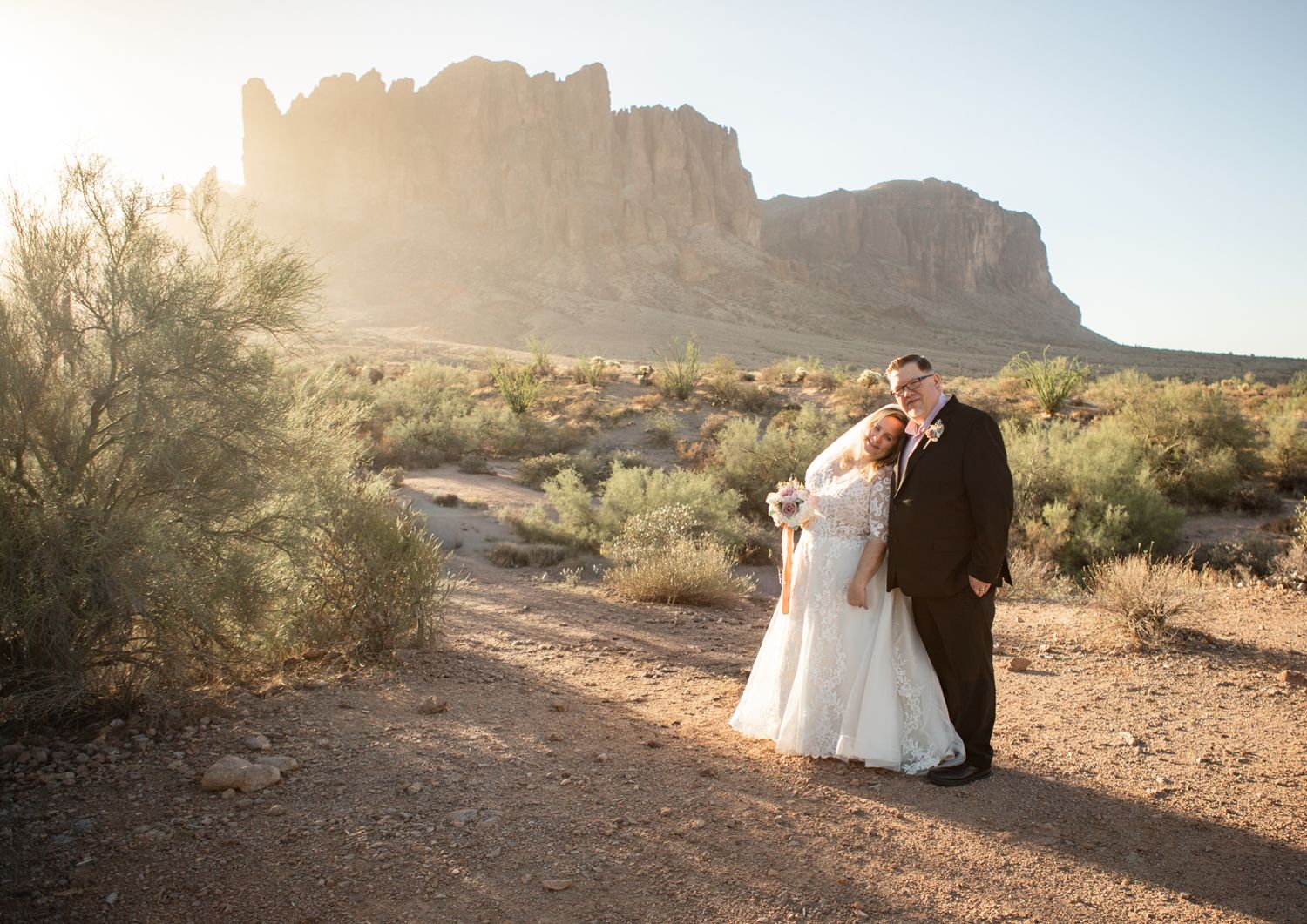 A romantic desert wedding portrait in front of the superstition mountains in warm sunlight.