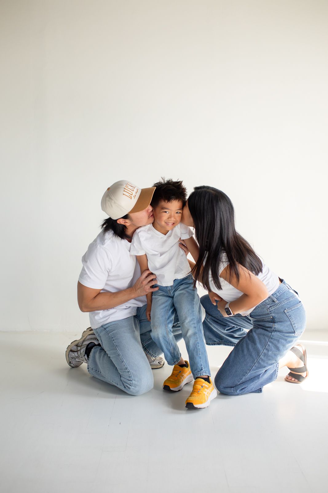 Family in matching white shirts and jeans sharing intimate moments in a minimalist studio setting at Letty Lume studio in Gilbert, Arizona.