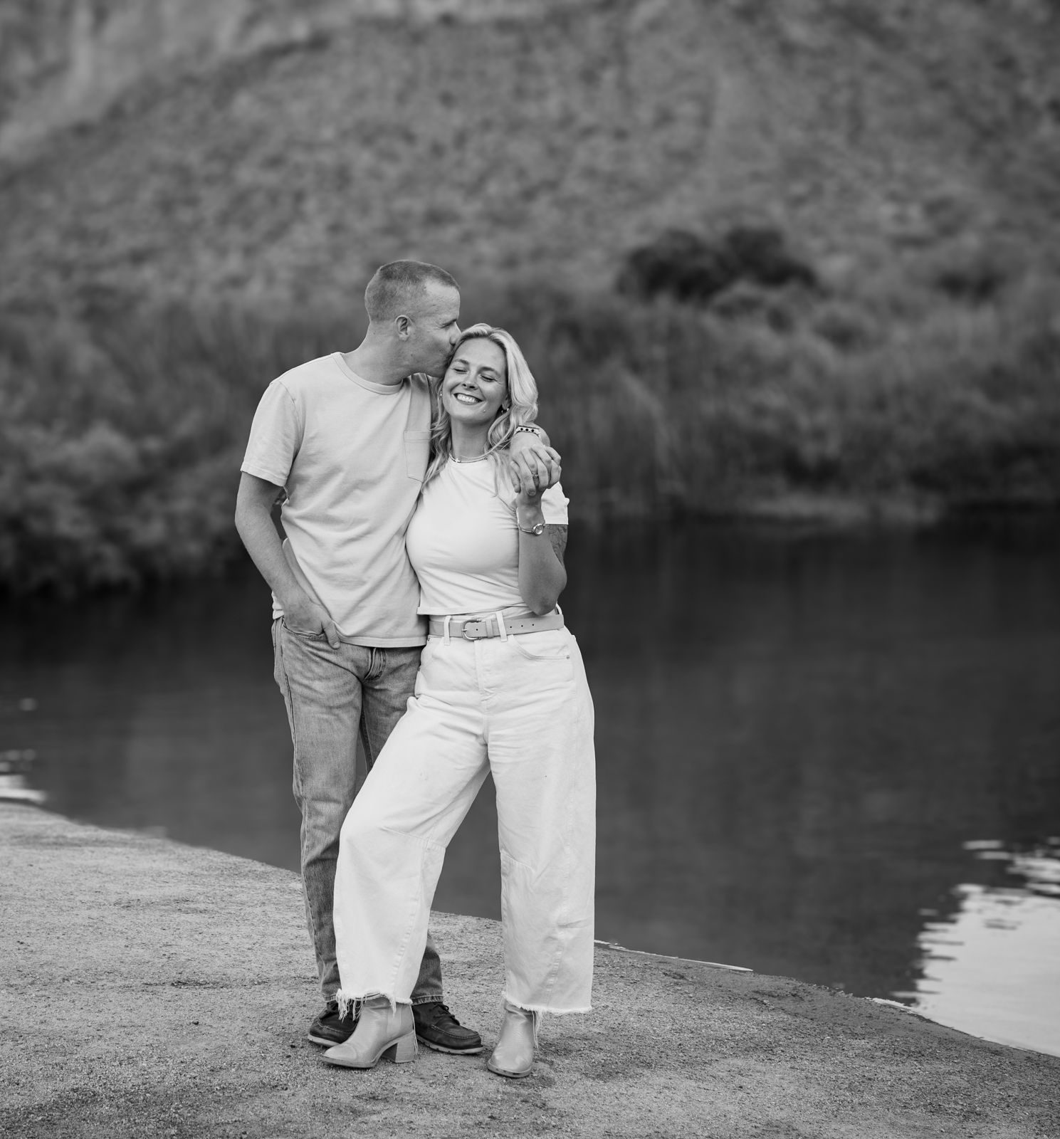 Black and white portrait of Al and Ben Carraway laughing together by a serene lake.
