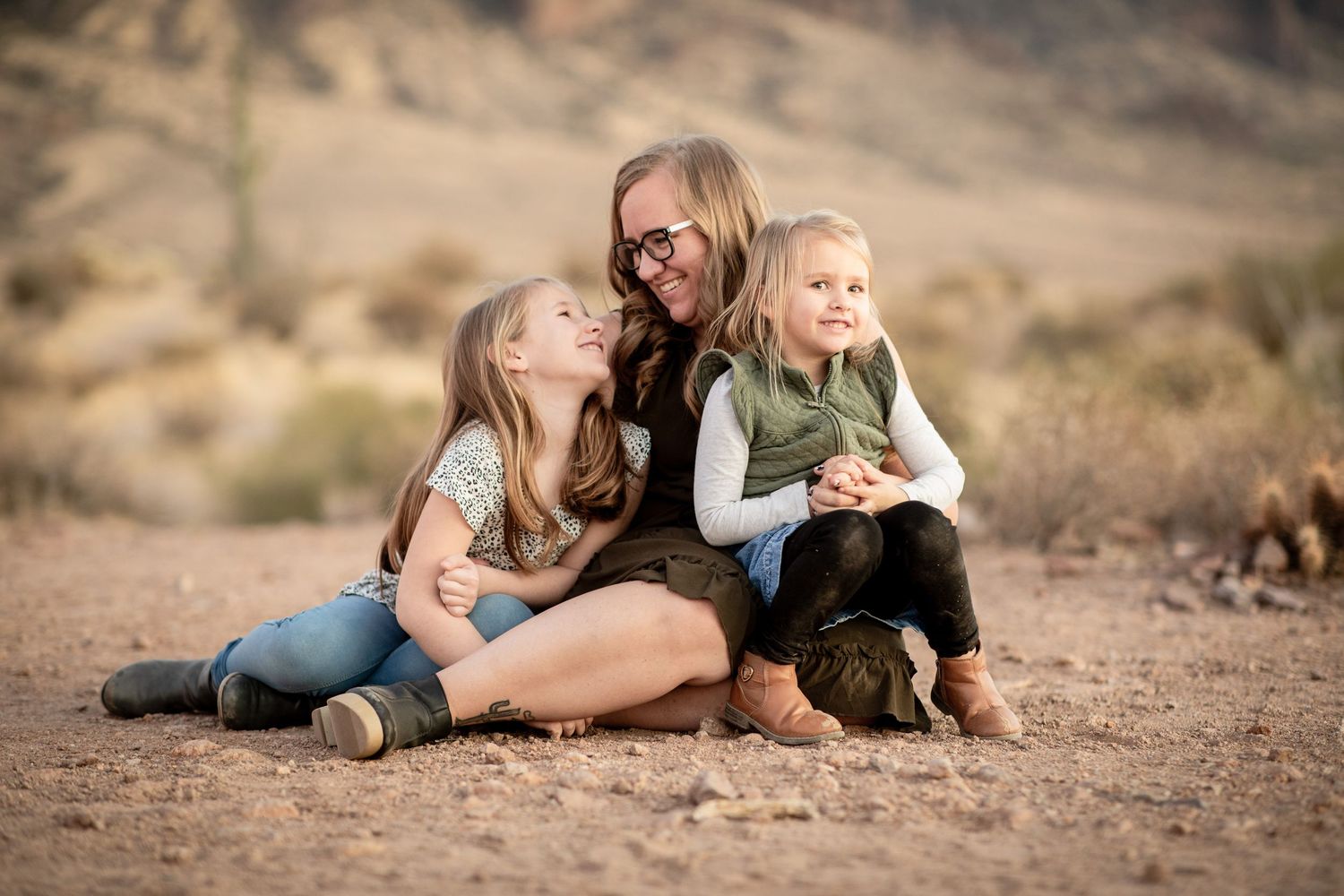 A couple lies in the desert sand with their dog during a romantic outdoor photo session at Lost Dutchman State park.