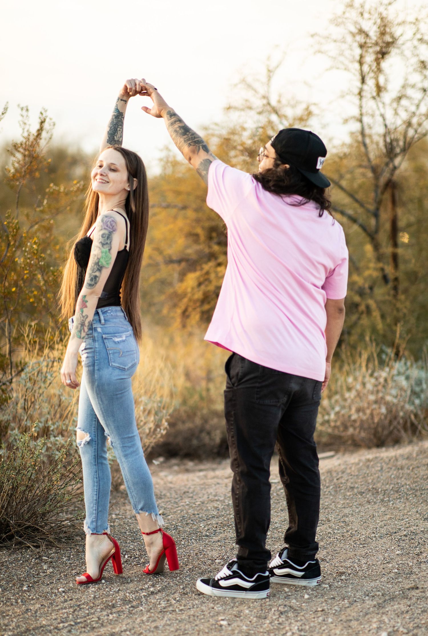 Two people in contrasting outfits dance together on a desert trail at dusk at Desert Arroyo Park in Mesa, Arizona.