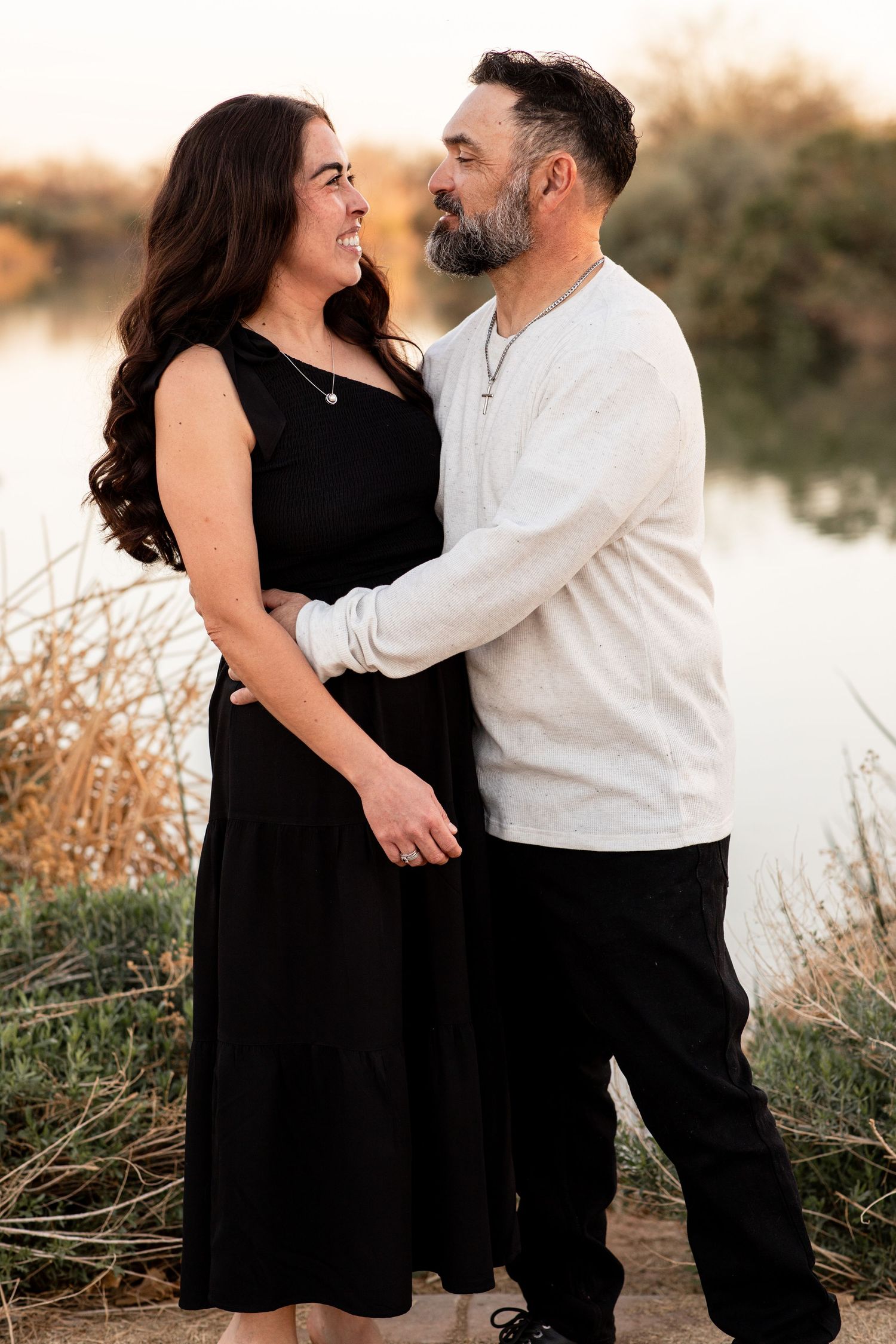 A couple embraces outdoors in a romantic photoshoot series, with her wearing black and him in white.