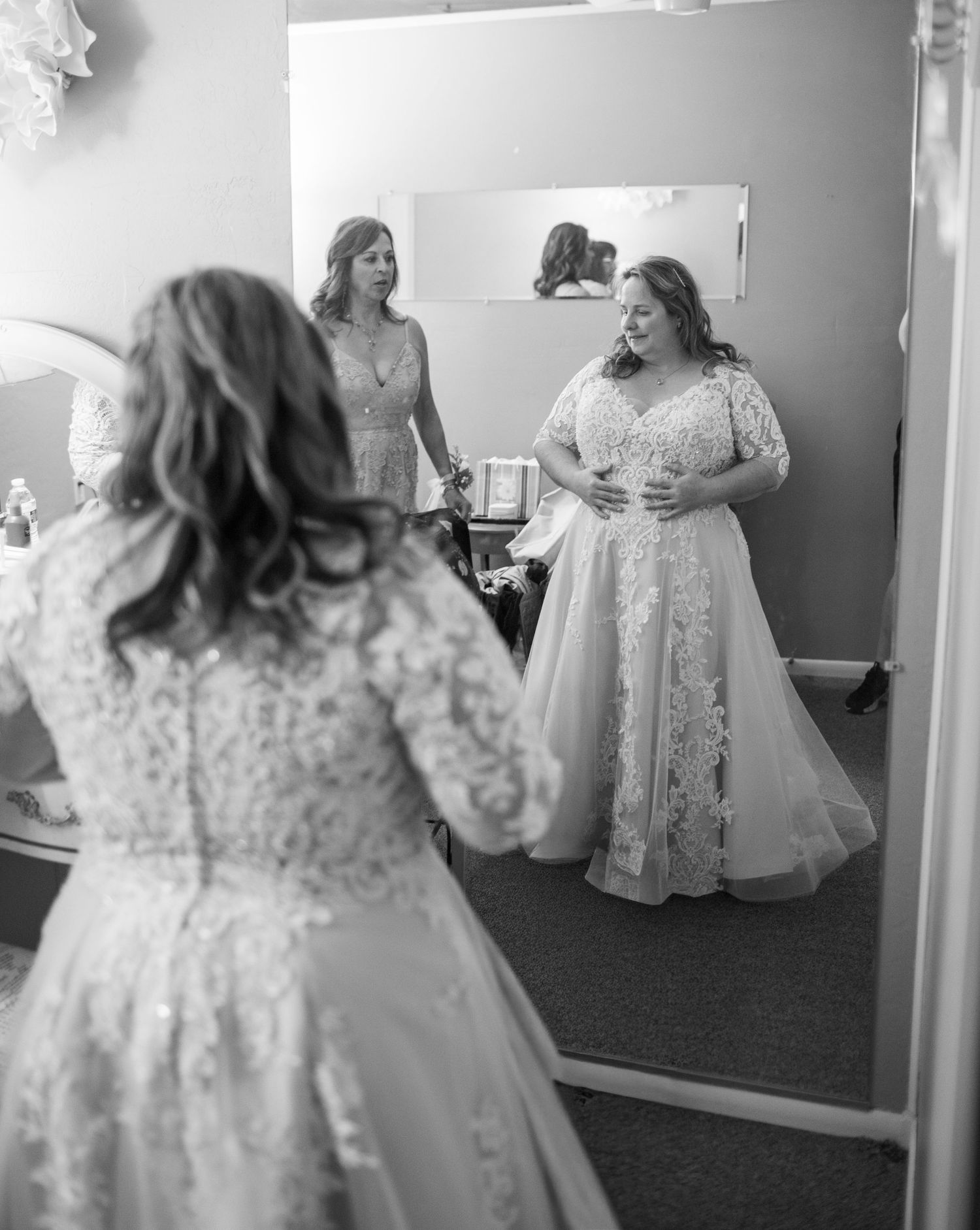 A bride in a lace wedding dress looks at her reflection in a mirror during a dress fitting at the Elvis Chapel in the Superstiton Mountains