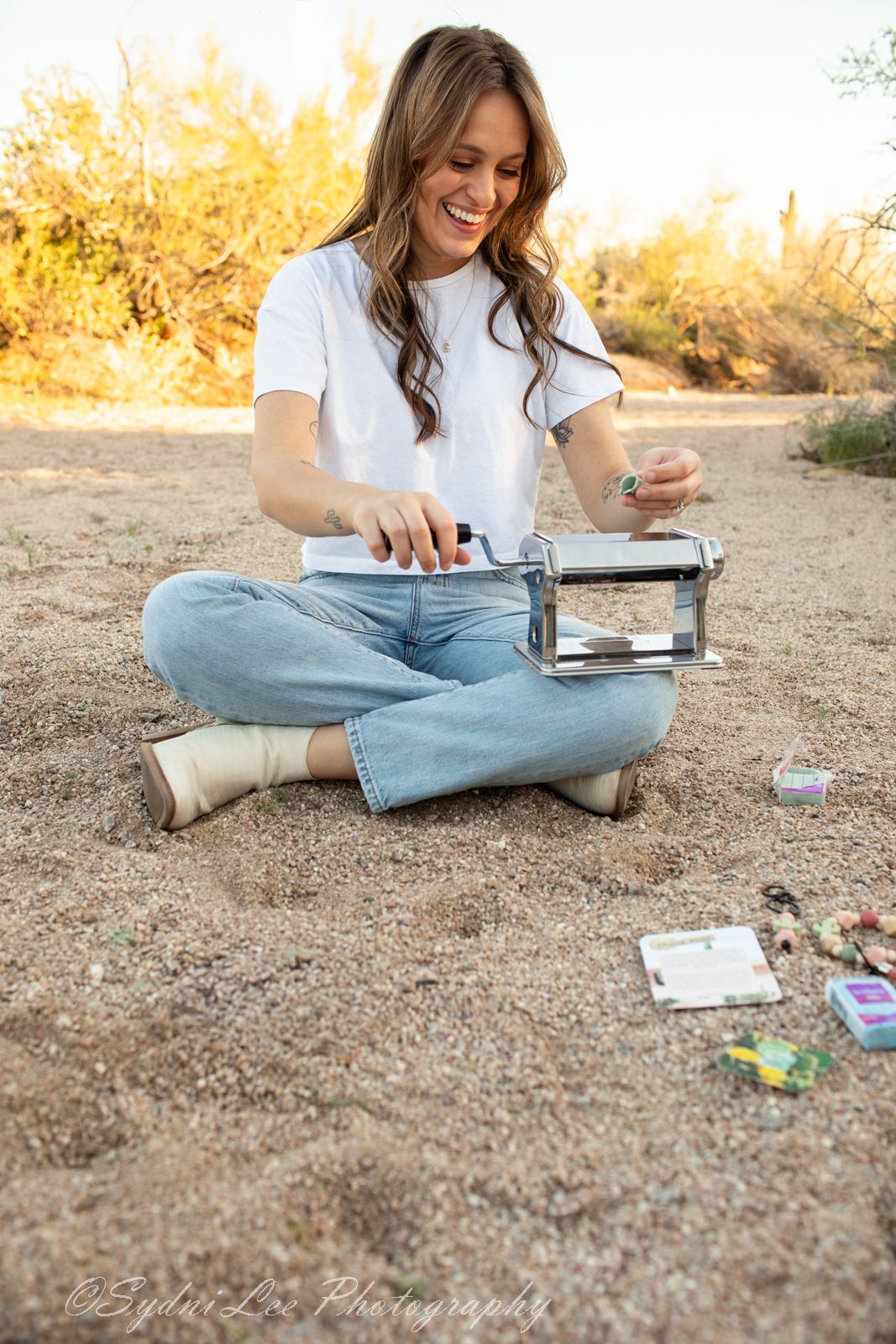 Person sitting on desert ground with books and papers spread out during sunset.