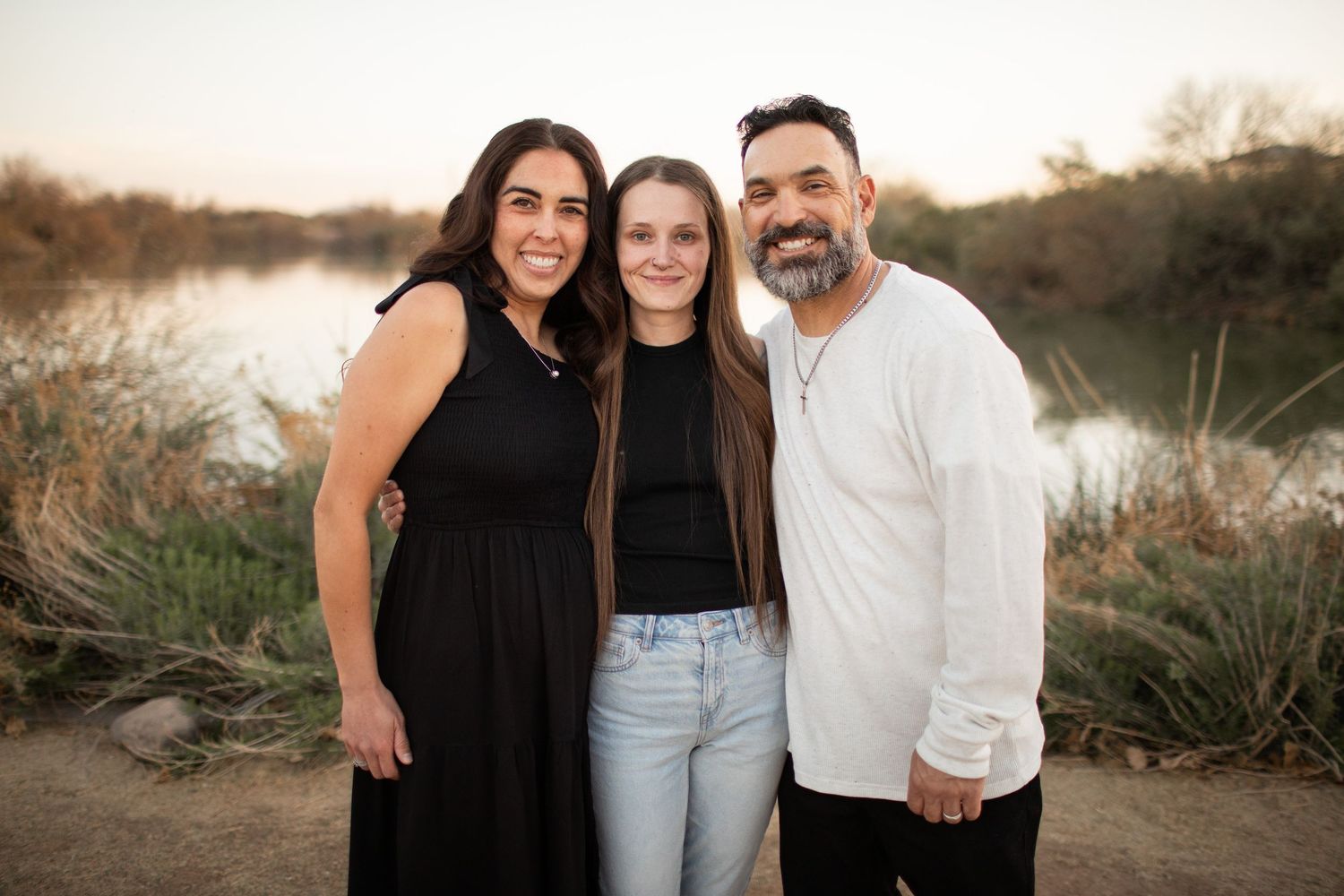 A family poses together outdoors during golden hour in a natural setting with tall grass and warm sunlight.