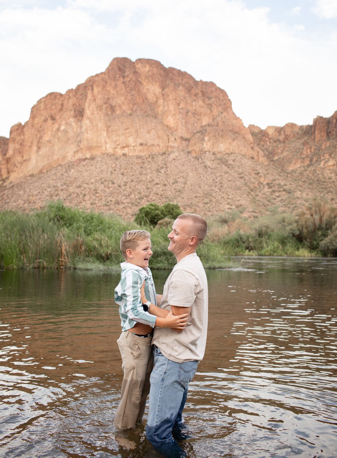 Children play together in a river with desert mountains and greenery in the background at Water Users recreational area.