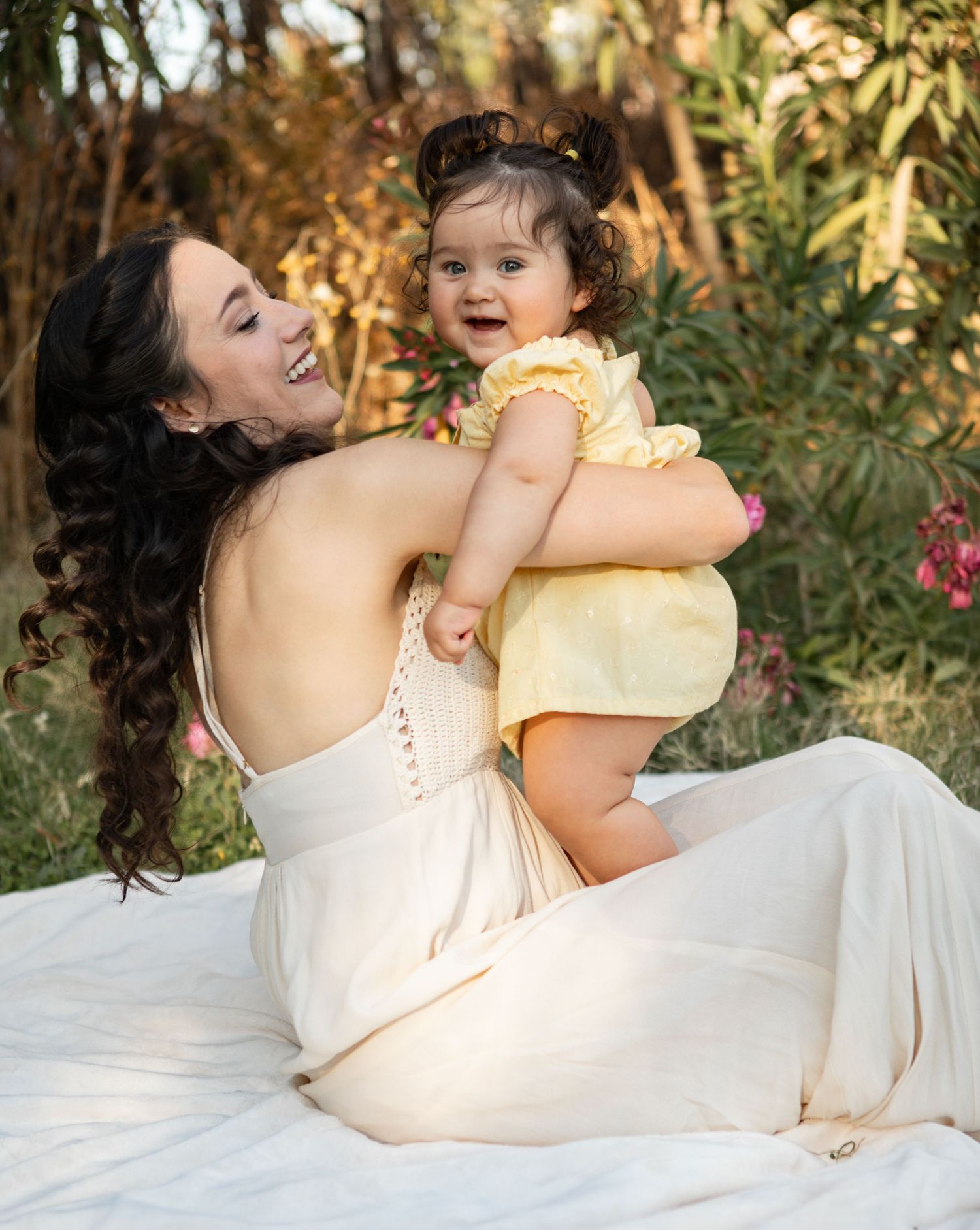 A series of tender moments captured on a white blanket with soft golden sunlight filtering through trees in the background at The Meadow.