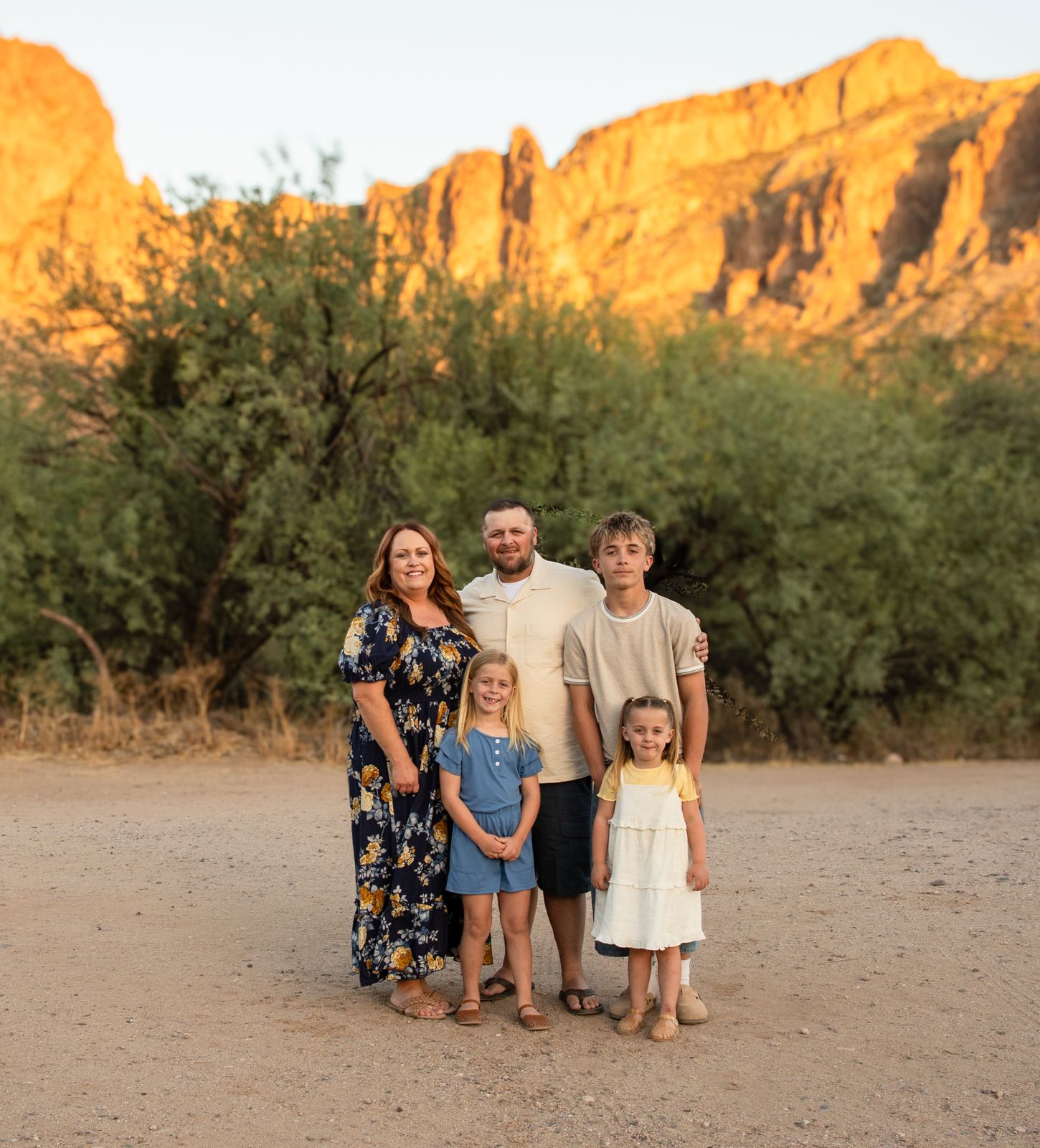 Family of five posing in desert landscape with golden red rock mountains at sunset in Arizona.