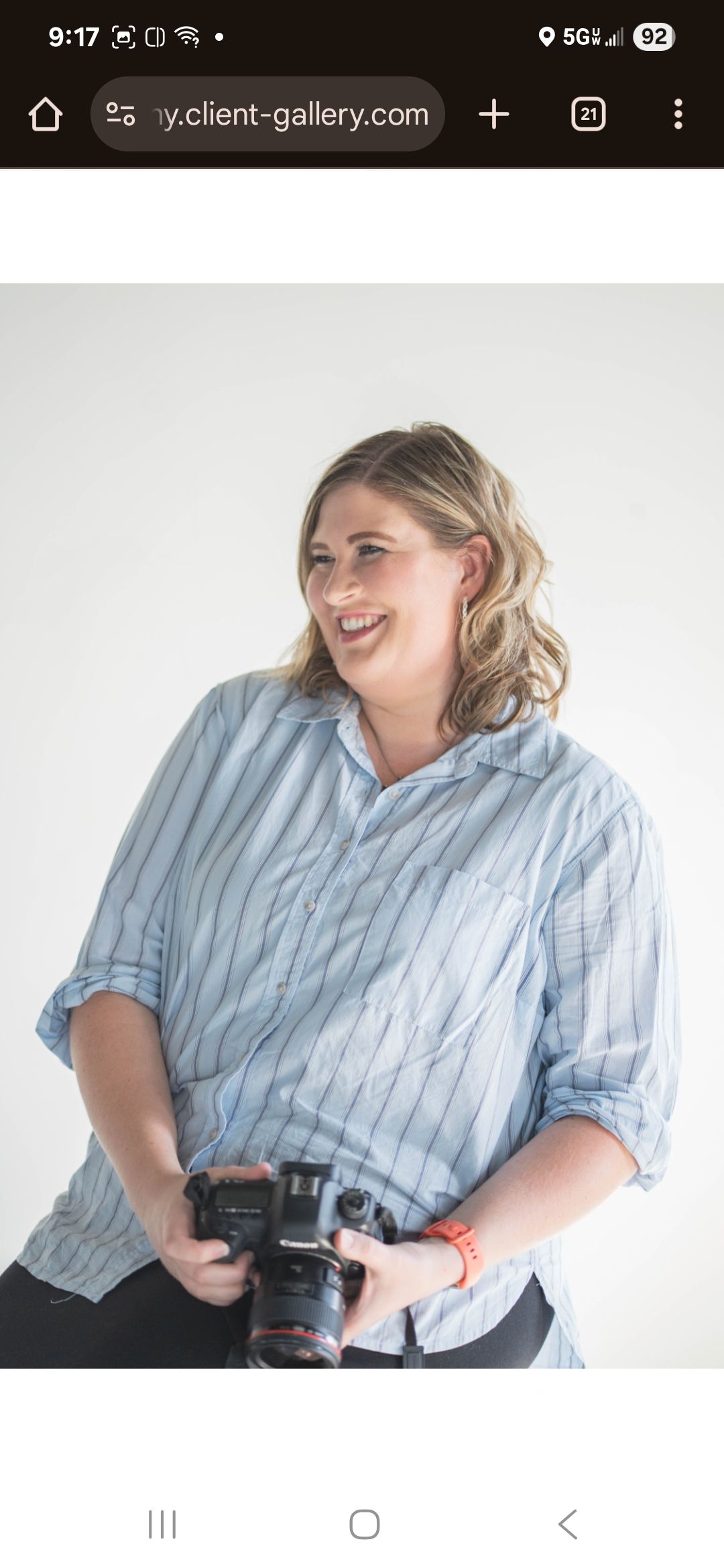 Professional photographer in a blue striped shirt laughing while holding a camera against white background.
