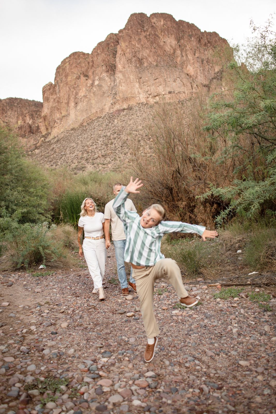 Family members walking and playing on rocky desert terrain with red cliffs in the background at Water Users recreational area.