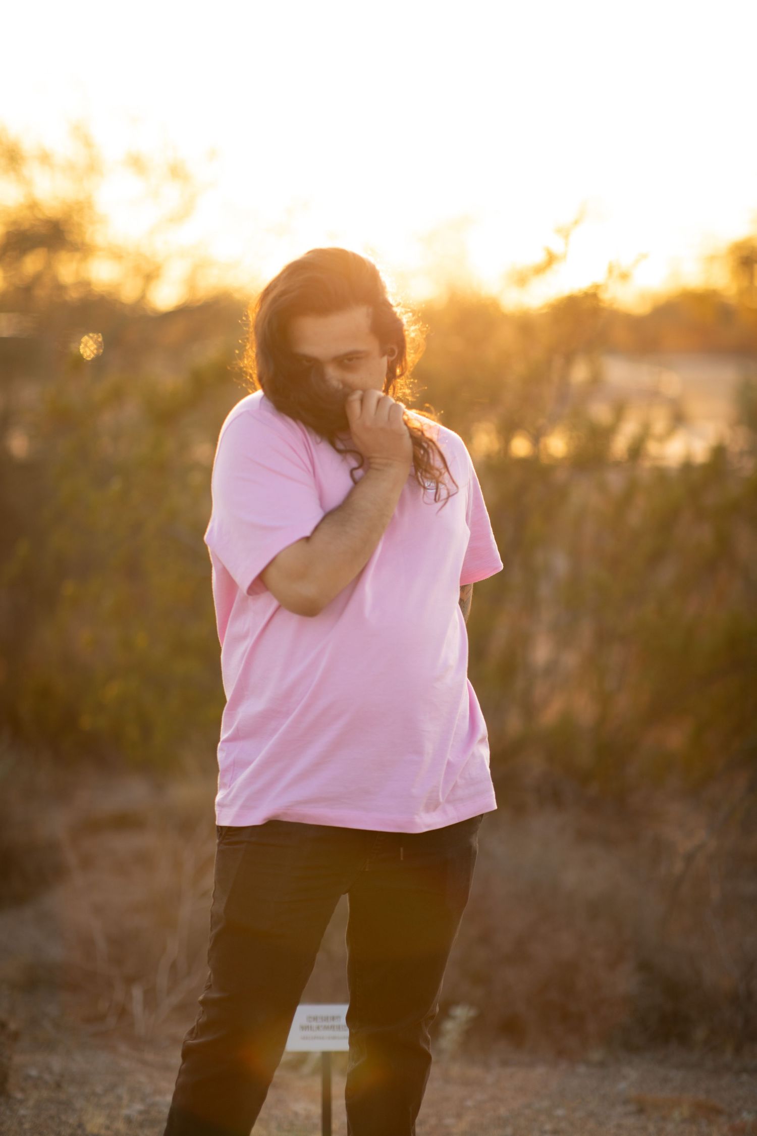 Person in pink shirt standing against golden sunset background in outdoor setting at Desert Arroyo Park in Mesa, Arizona.