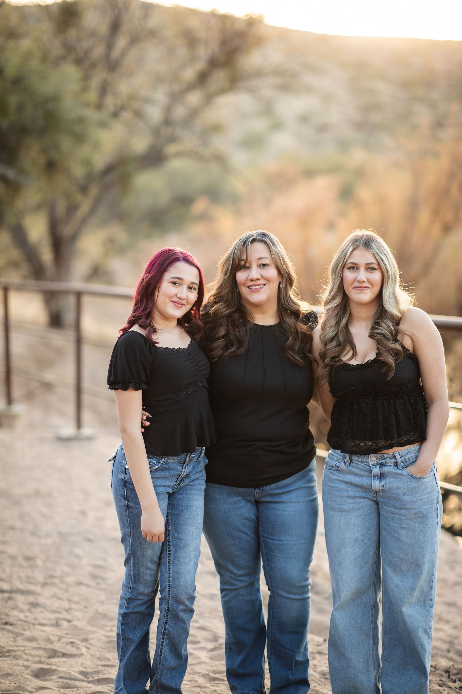 Three women in casual denim standing together on desert trail near the Salt River, Arizona at sunset.