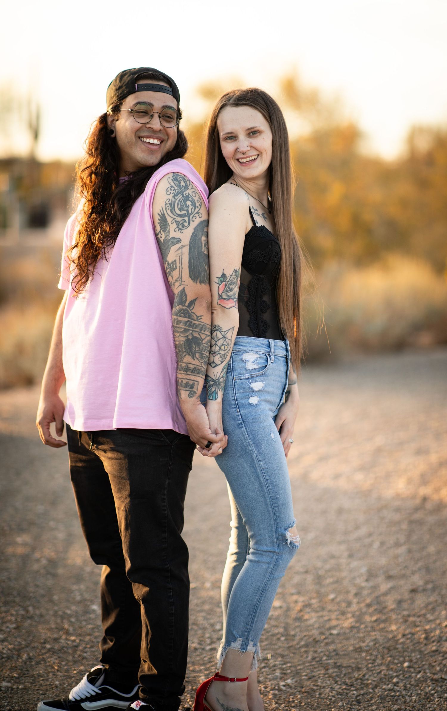 Two people in casual attire pose together outdoors during golden hour sunset in a desert landscape at Desert Arroyo Park in Mesa, Arizona.