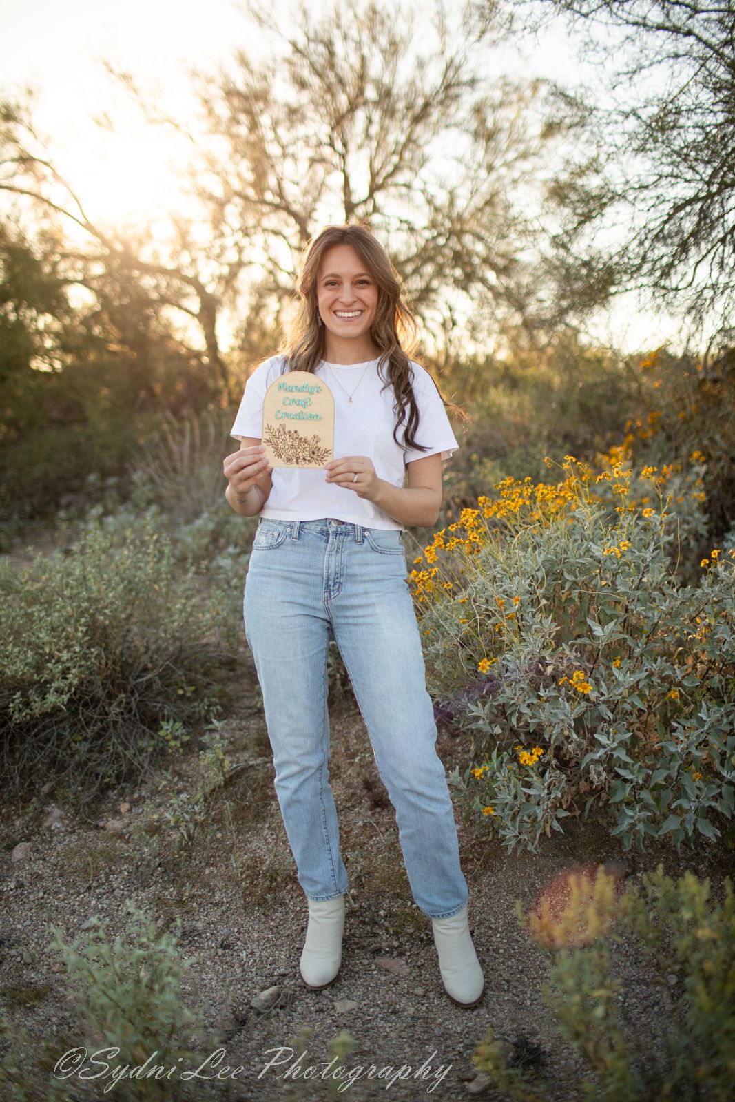 Person in casual white top and light denim stands among desert wildflowers during golden hour photography session.