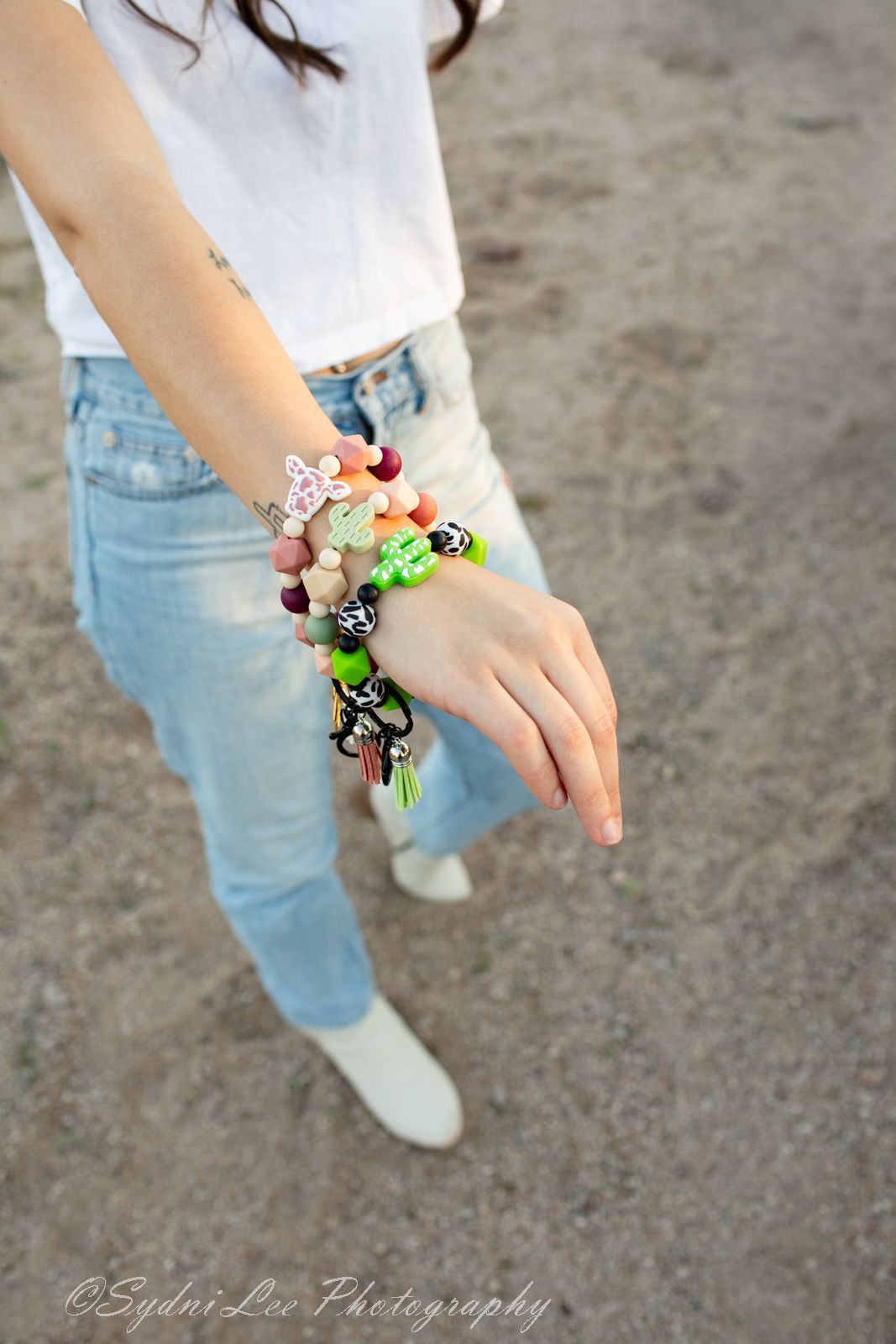 Close-up view of hands wearing colorful charm bracelets and rings with light denim jeans.