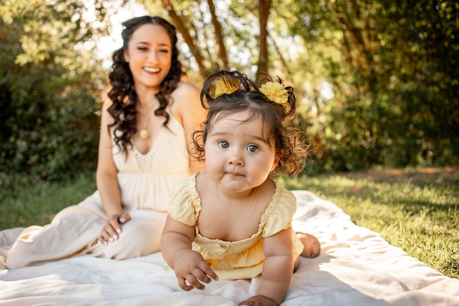 A family enjoys quality time together on a picnic blanket in a sun-dappled park during golden hour at The Meadow in Mesa.