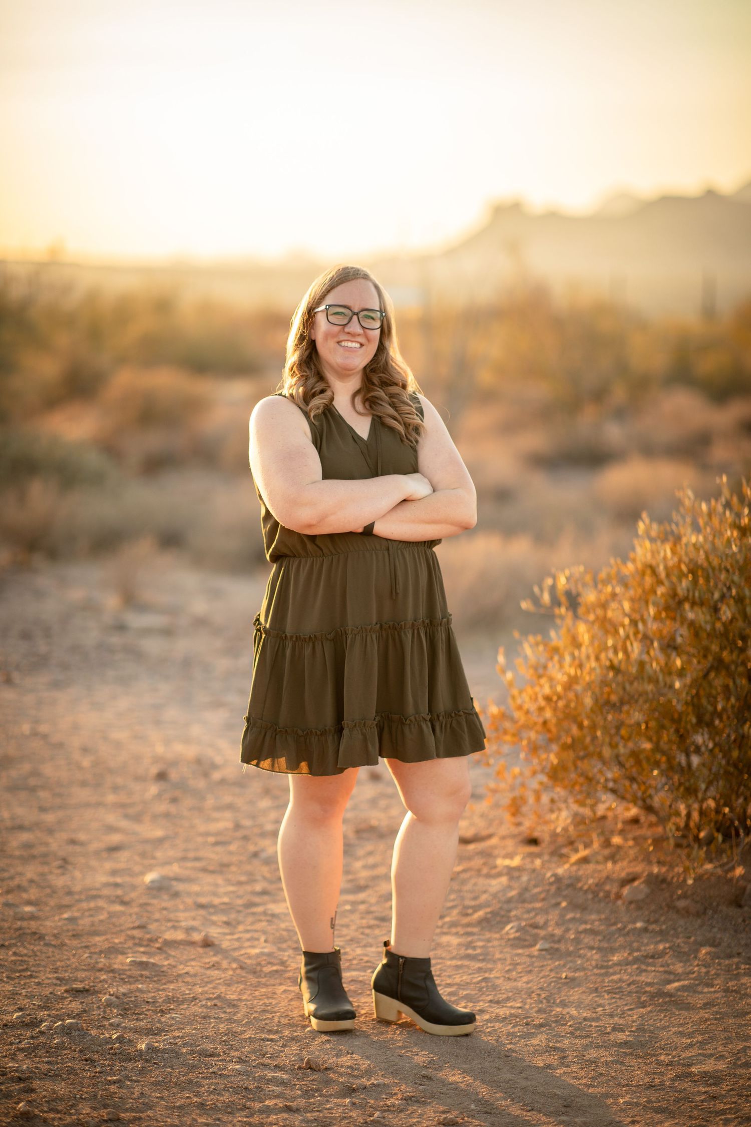 A person wearing a black dress poses in a desert landscape at golden hour with warm sunlight filtering through at Lost Dutchman State park.