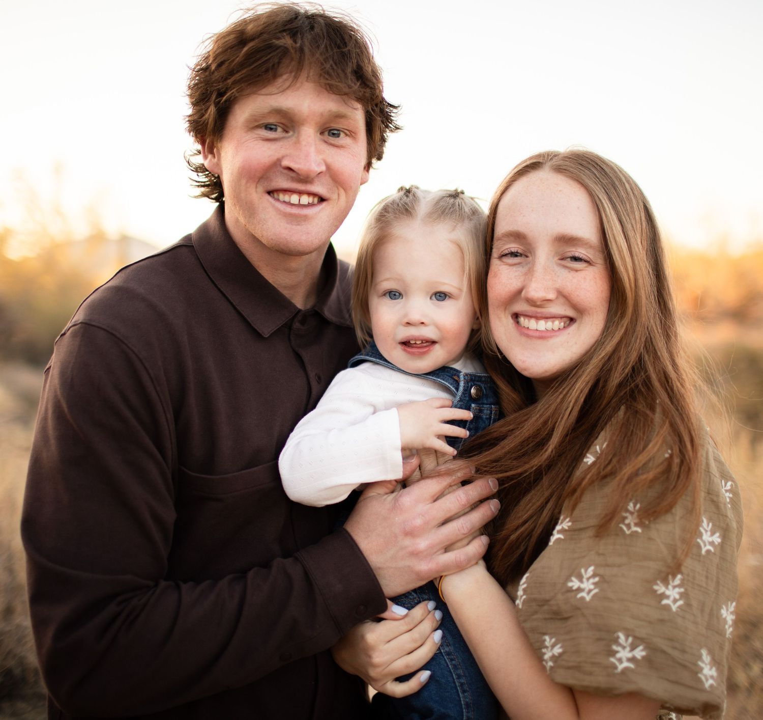 Family enjoying a warm sunset moment together outdoors in casual attire during an autumn photoshoot.