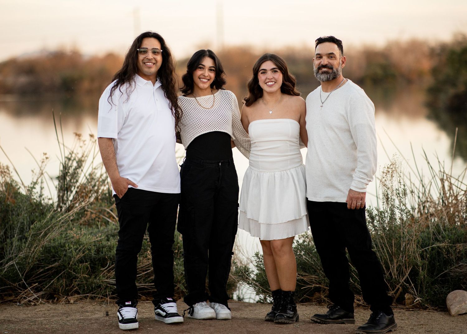 A group in coordinated white and black outfits poses together outdoors at sunset in a natural setting.