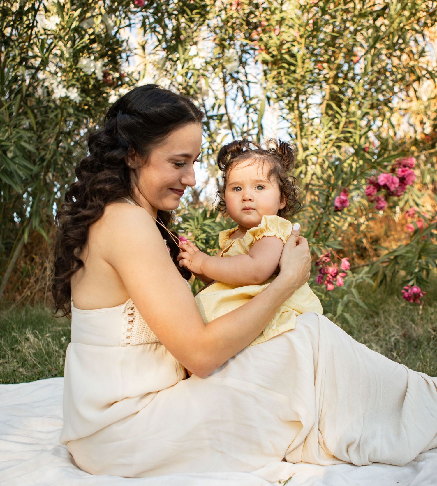 A mother and child share a tender moment together outdoors among autumn foliage in white and cream-colored attire at The Meadow in Mesa.