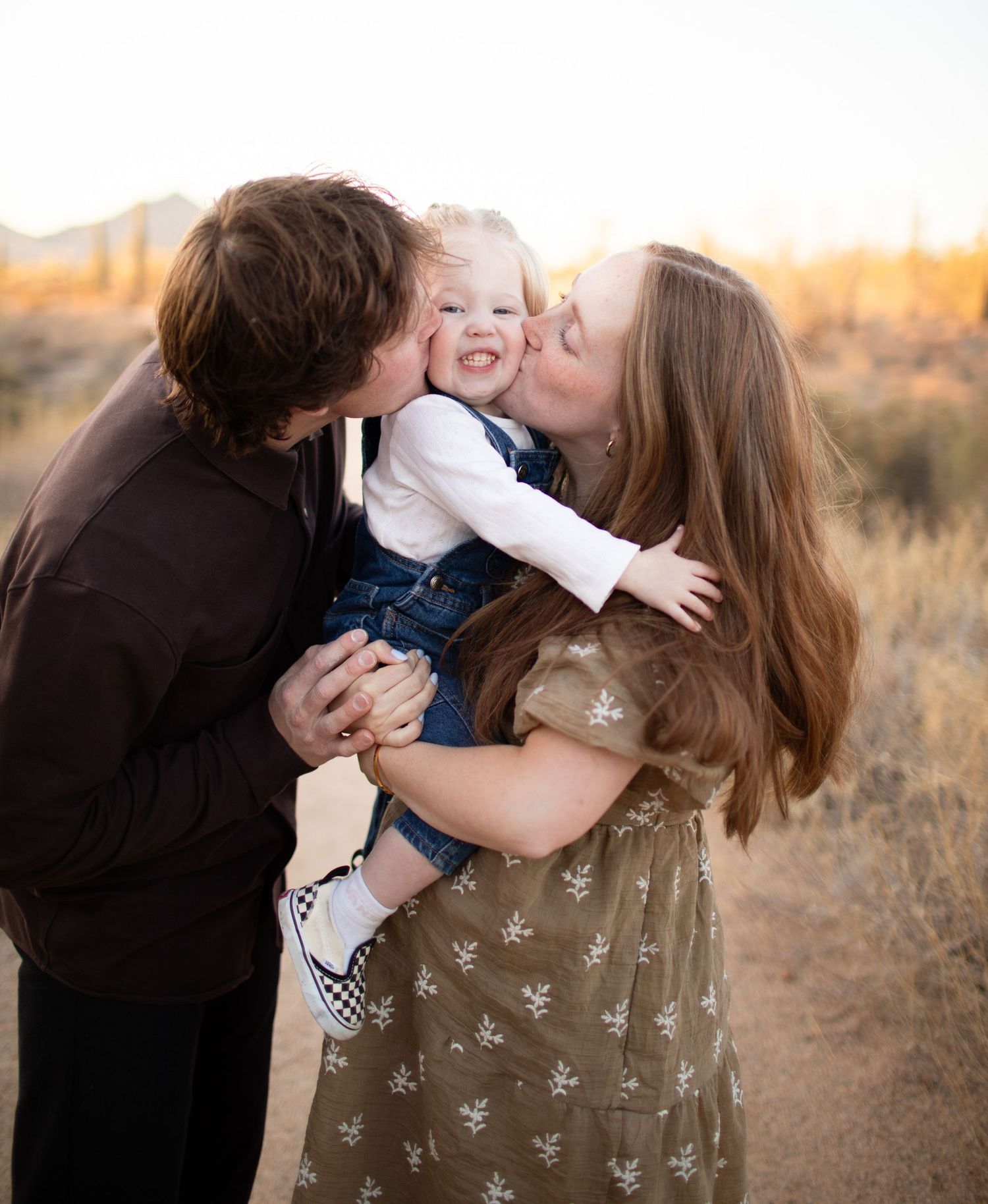 A family shares tender moments in a field at sunset as they embrace and play together.