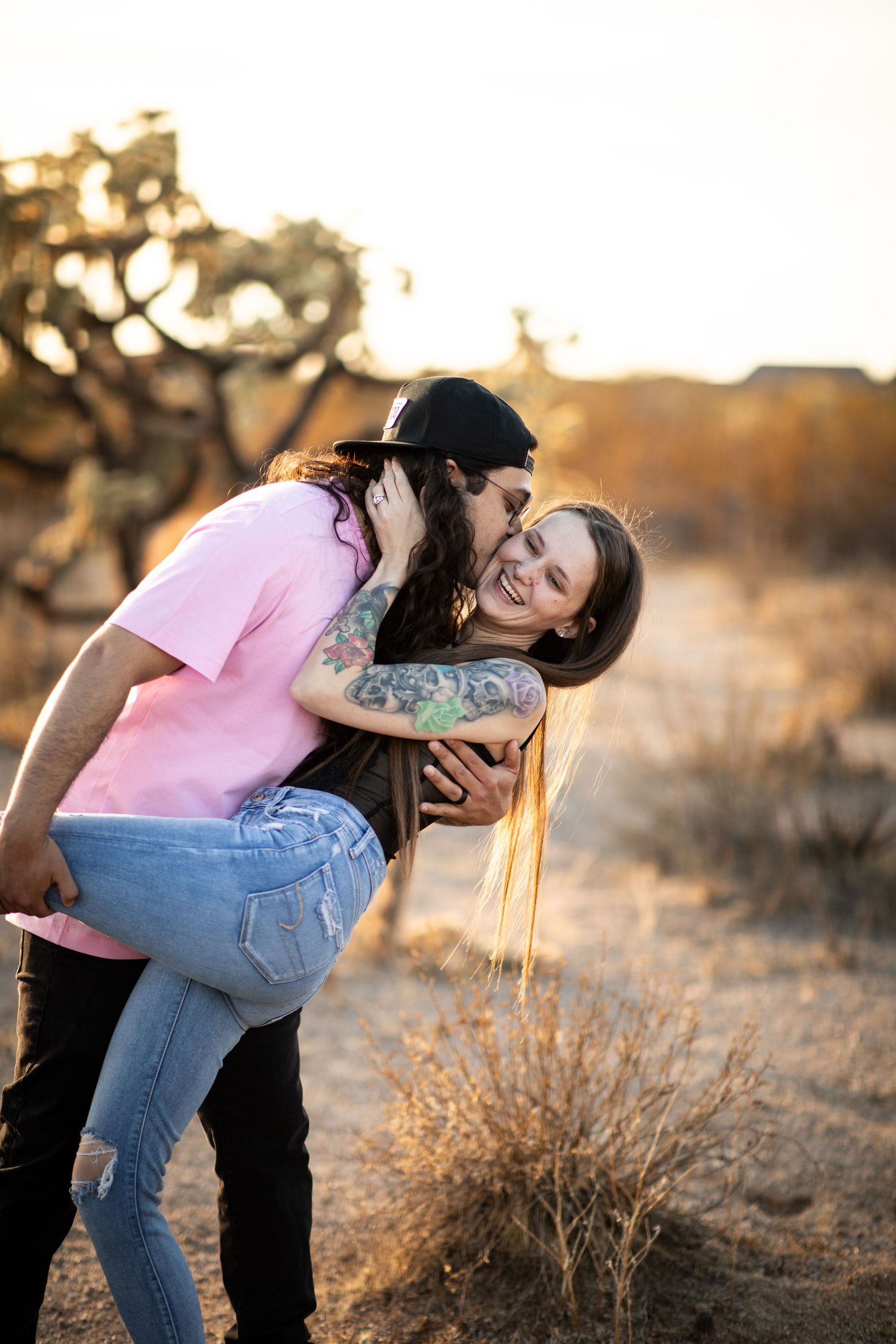 A romantic couple embraces and laughs together during golden hour in a desert landscape at Desert Arroyo Park in Mesa, Arizona.
