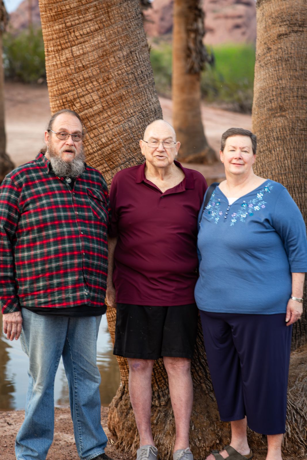 Three people standing together between palm trees in an outdoor setting near water in Papago Park in Phoenix, AZ.