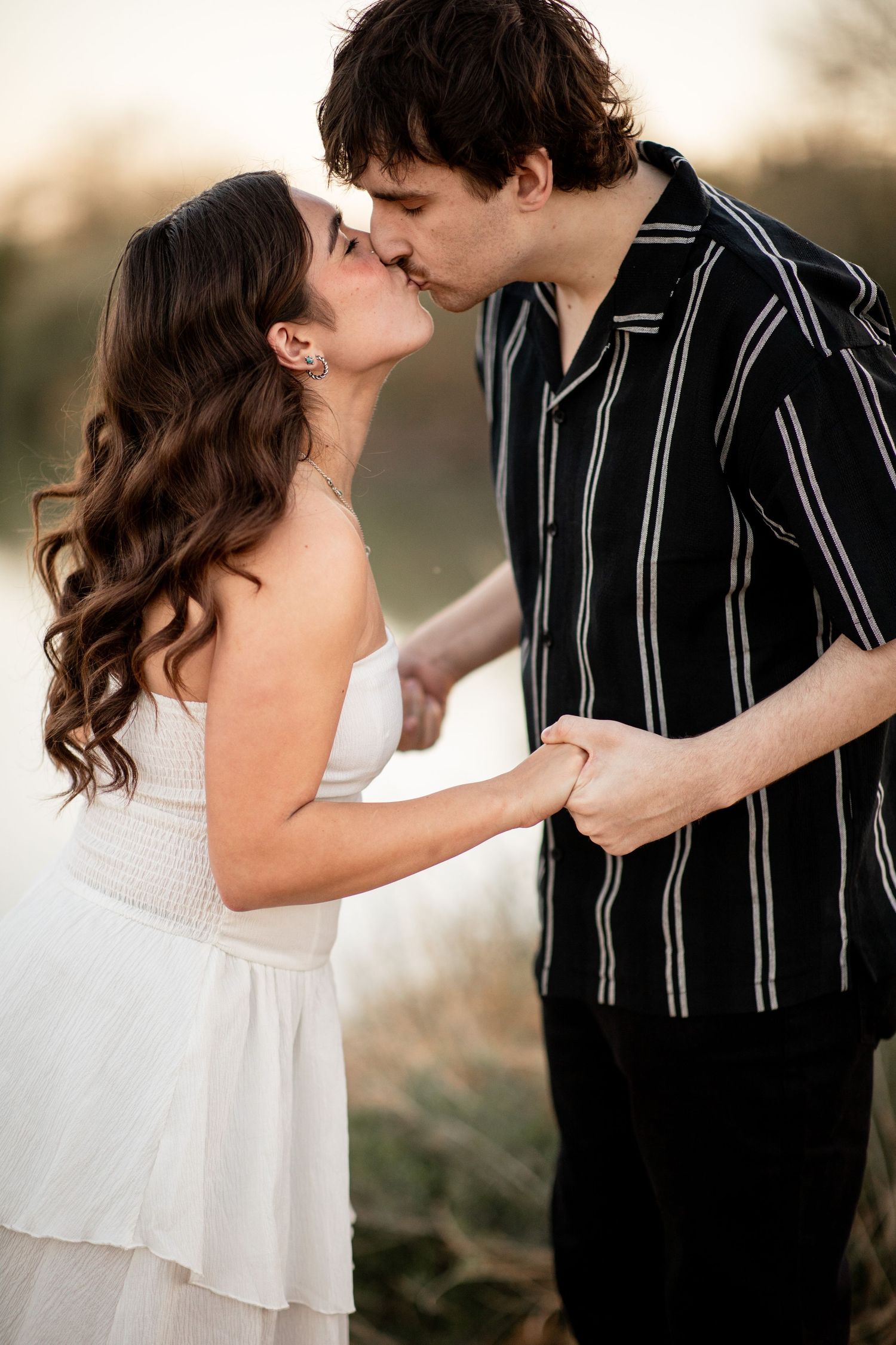A romantic couple in black and white attire share tender moments during an outdoor photo session at sunset.