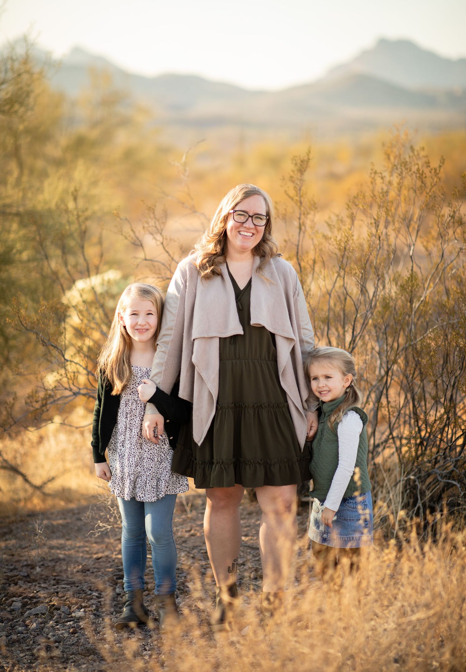 A portrait of three people standing together against a desert mountain landscape at sunset in the superstitions.