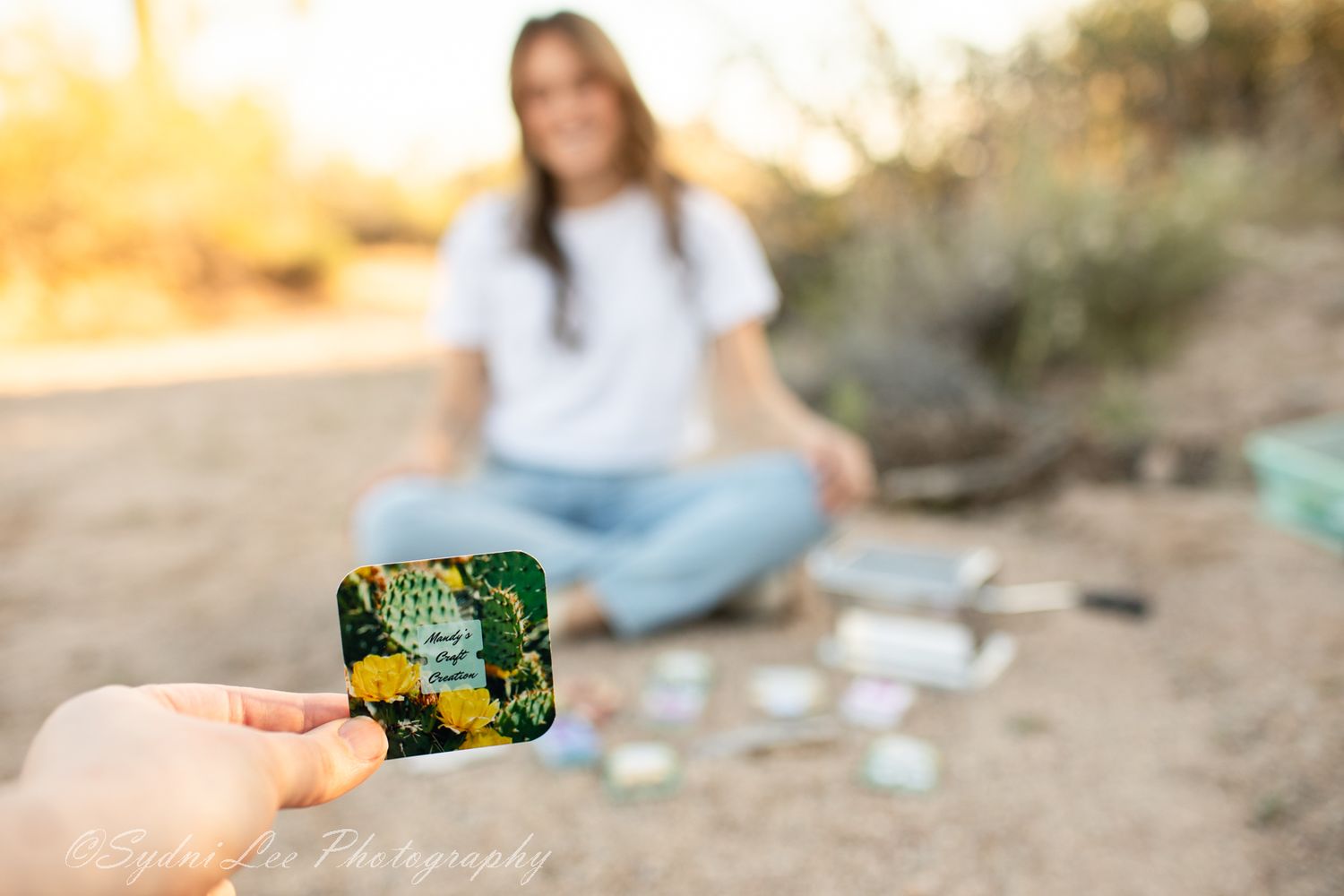 Hands holding colorful items against a desert sunset background.