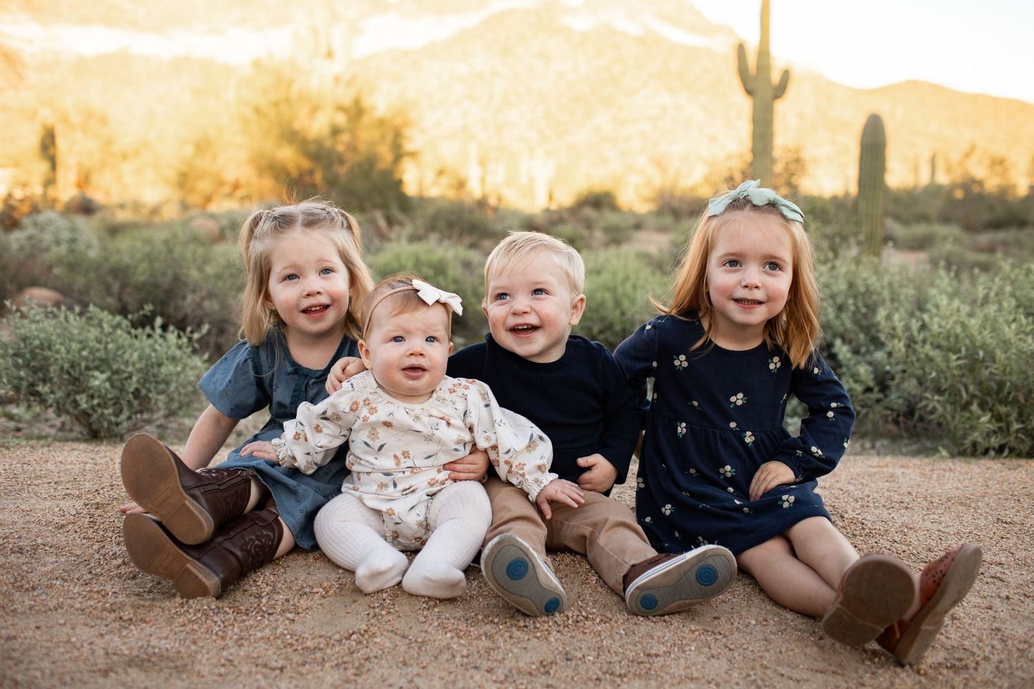 Four children sitting together and laughing on the ground at Merkle Trail with mountains and cacti in the background.