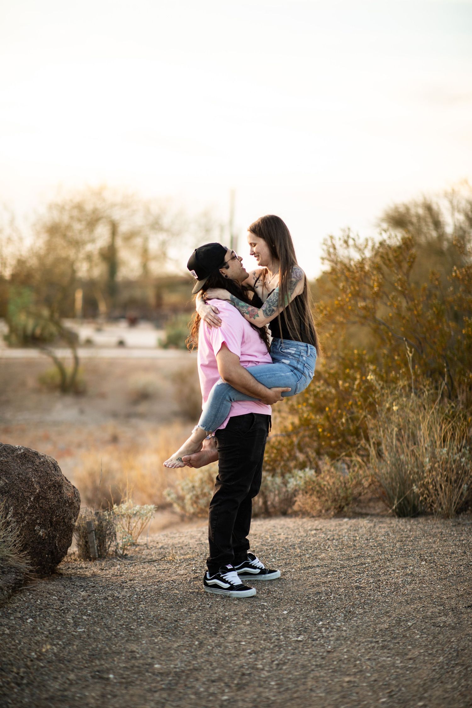 A couple embraces in a romantic dance-like pose against a desert landscape at sunset at Desert Arroyo Park in Mesa, Arizona.