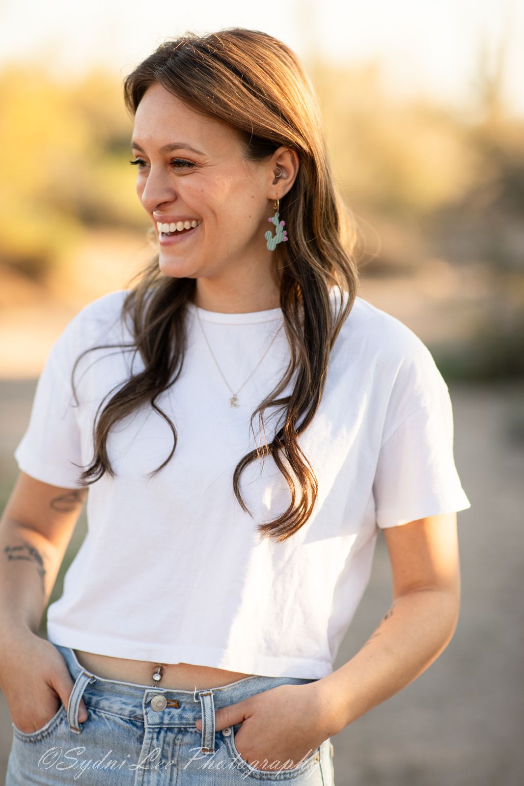 Person in white crop top and jeans smiles while standing outdoors during golden hour.