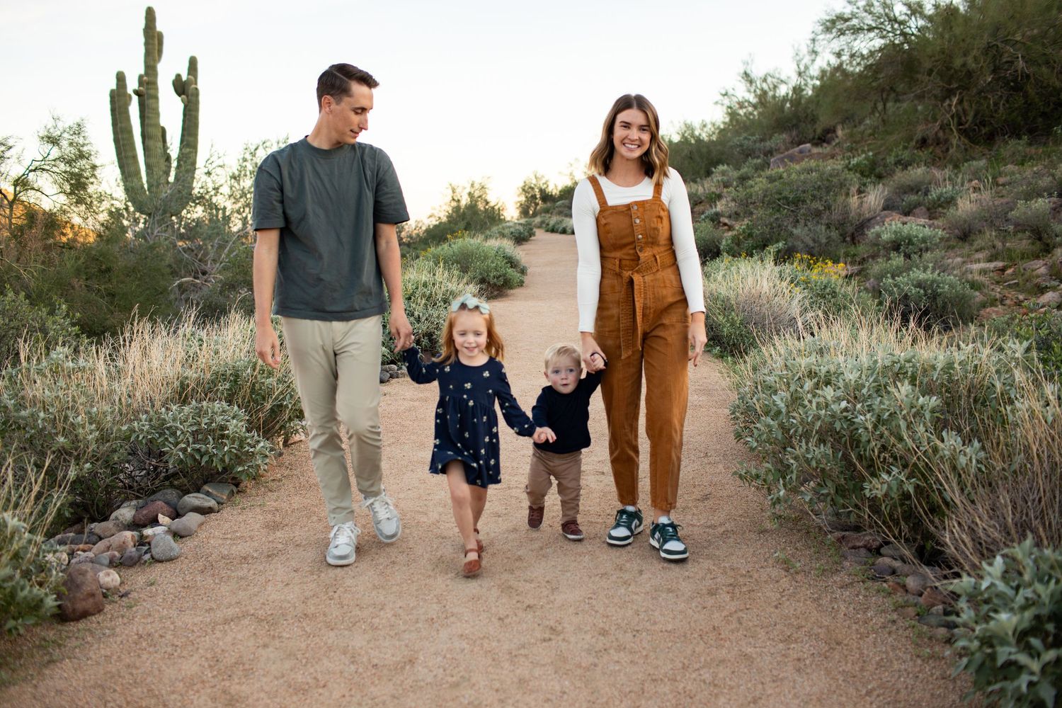 A family walks together on a desert trail surrounded by cacti and desert plants during golden hour on the Merkle Trail in Mesa, Arizona.