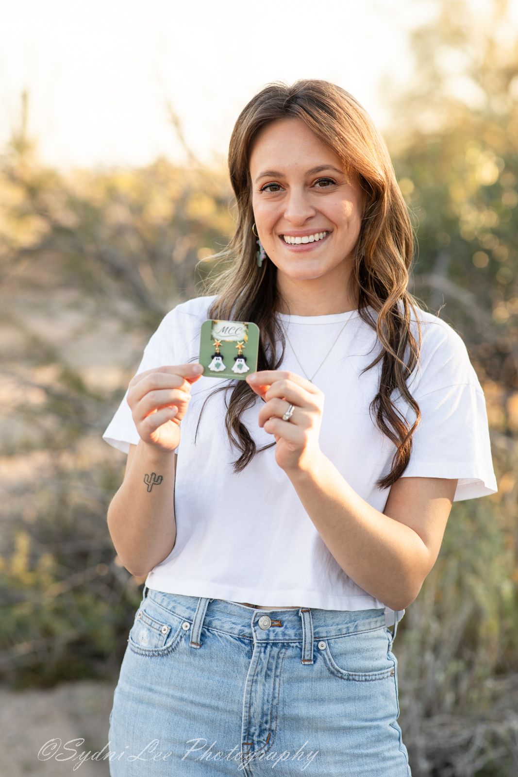 A casual outdoor photoshoot featuring a white t-shirt and cactus-themed accessories in a desert setting.