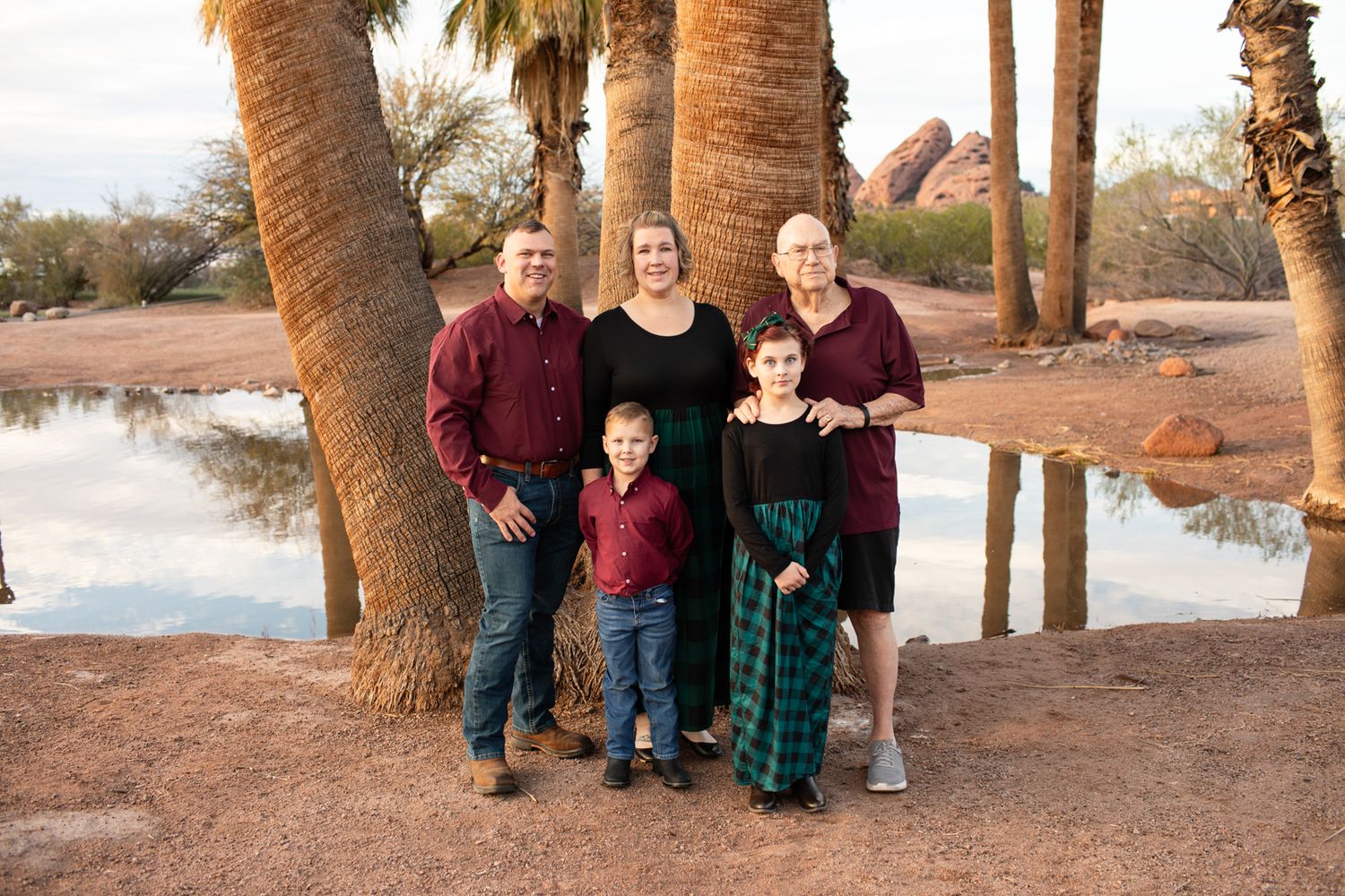 A group poses together by palm trees in a desert landscape at sunset with a water feature in the background in Papago Park in Phoenix, AZ.