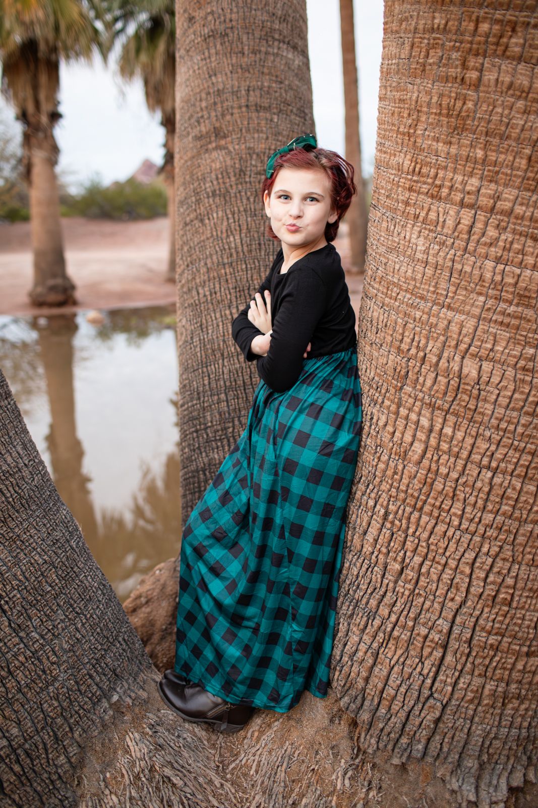 A person in a green plaid flannel shirt poses against palm tree trunks in a series of artistic outdoor photos in Papago Park in Phoenix, AZ.