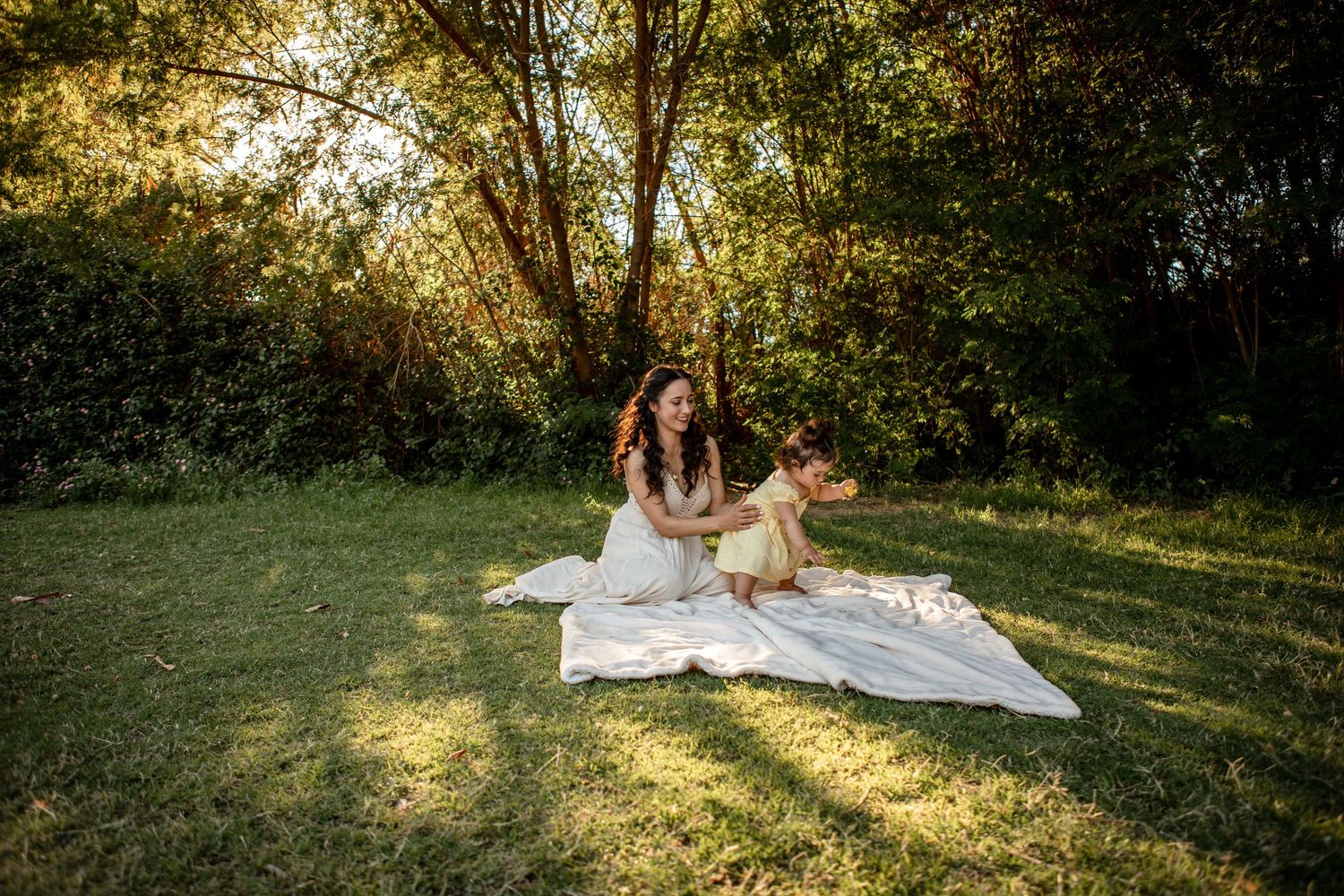 A person in a white dress poses gracefully on a blanket in a sunlit meadow during golden hour at The Meadow in Mesa.