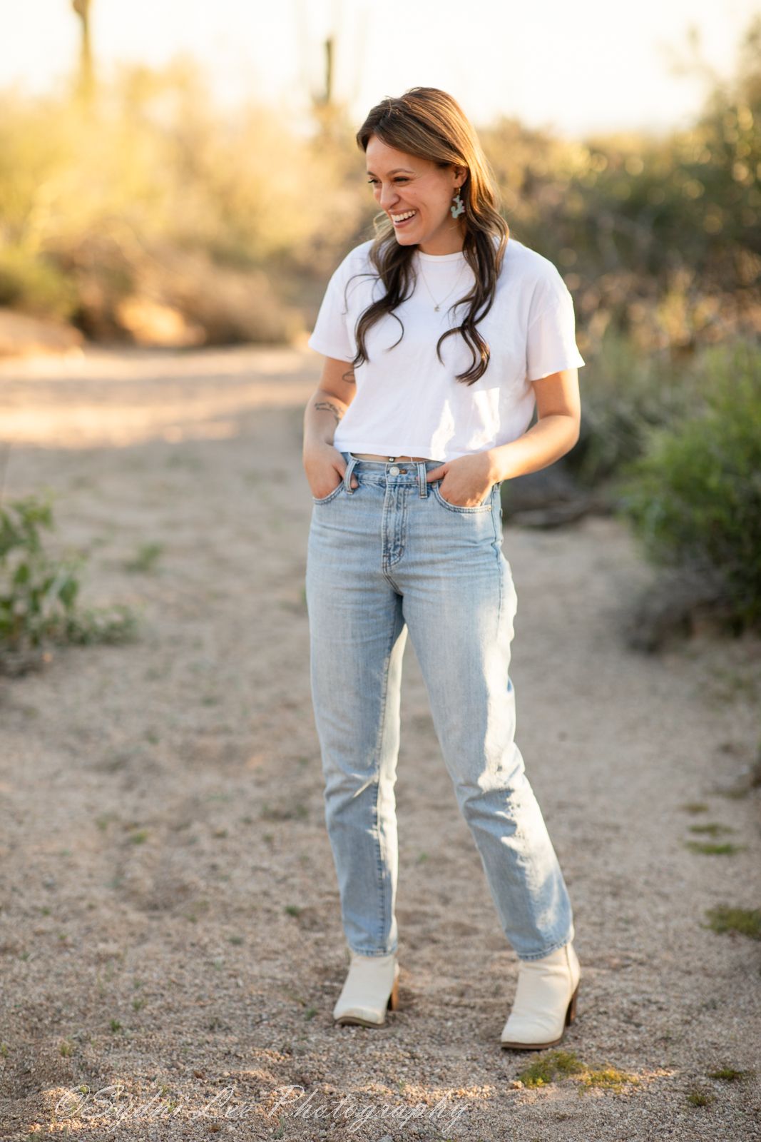 White boots and light denim jeans styled on a desert trail with brush in the background.
