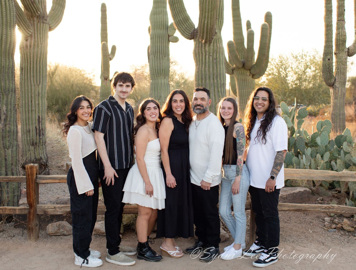 A group poses for photos among tall saguaro cacti in the Arizona desert during golden hour.
