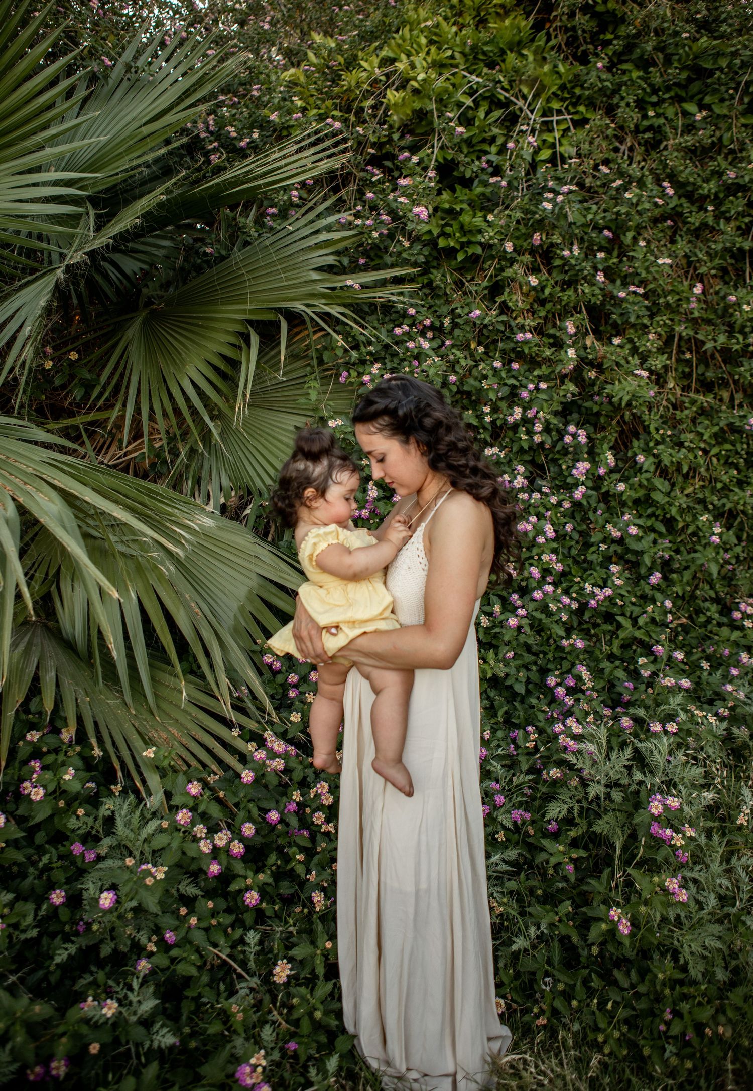 A tender moment captured between parent and child against a lush backdrop of palm fronds and pink flowers at The Meadow in Mesa.