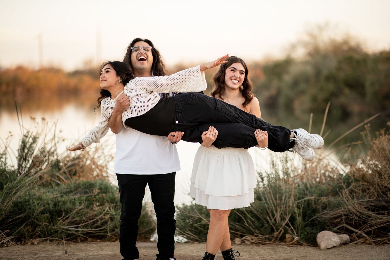 A joyful couple in black and white outfits laughs together during a sunset photoshoot by the water.