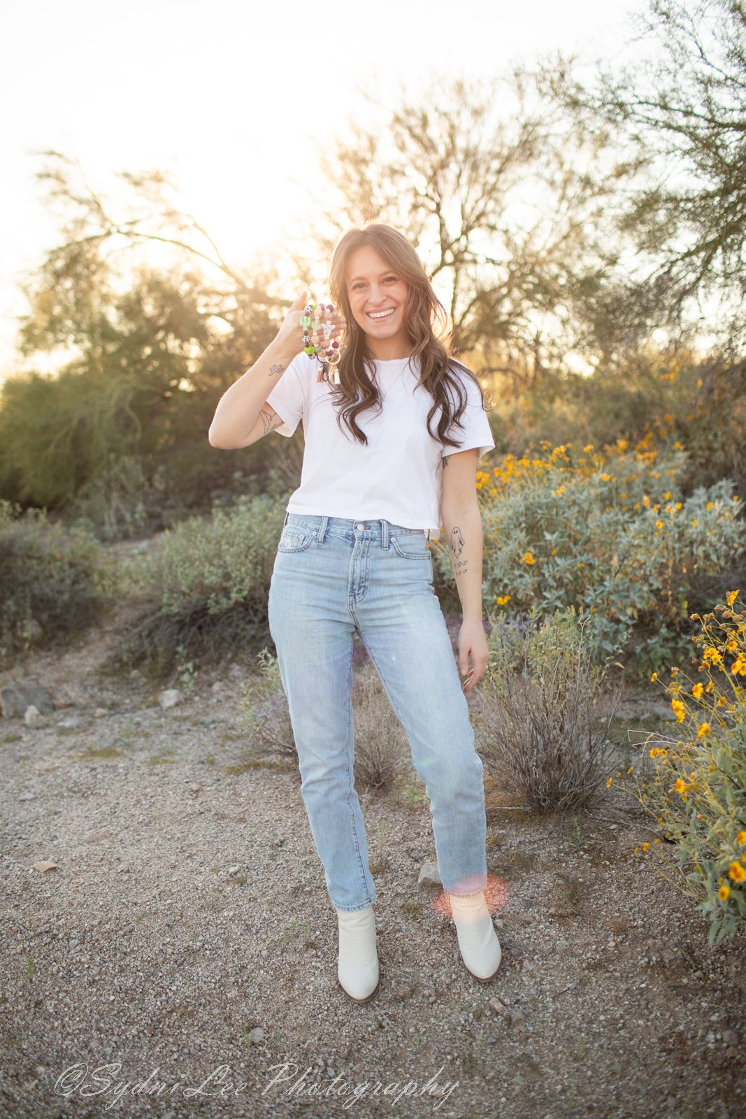 Person in casual white tee and jeans poses against desert landscape with yellow wildflowers.