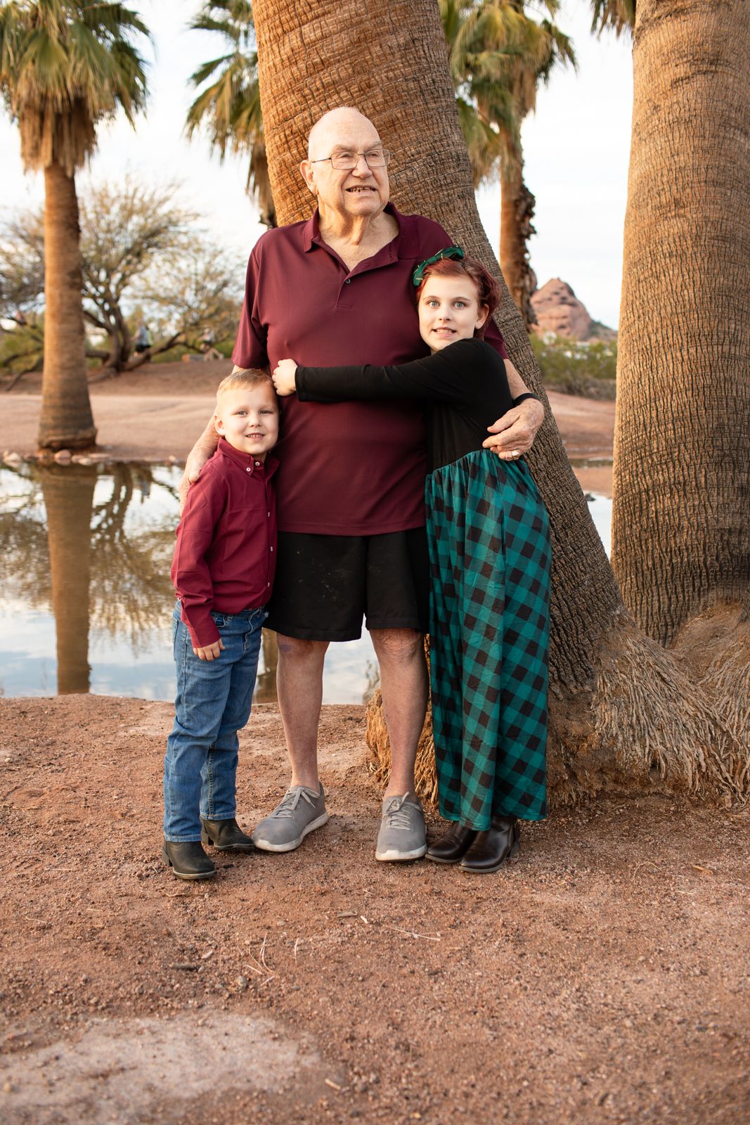 Family members in burgundy and plaid attire pose together among tall palm trees in Papago Park in Phoenix, AZ.