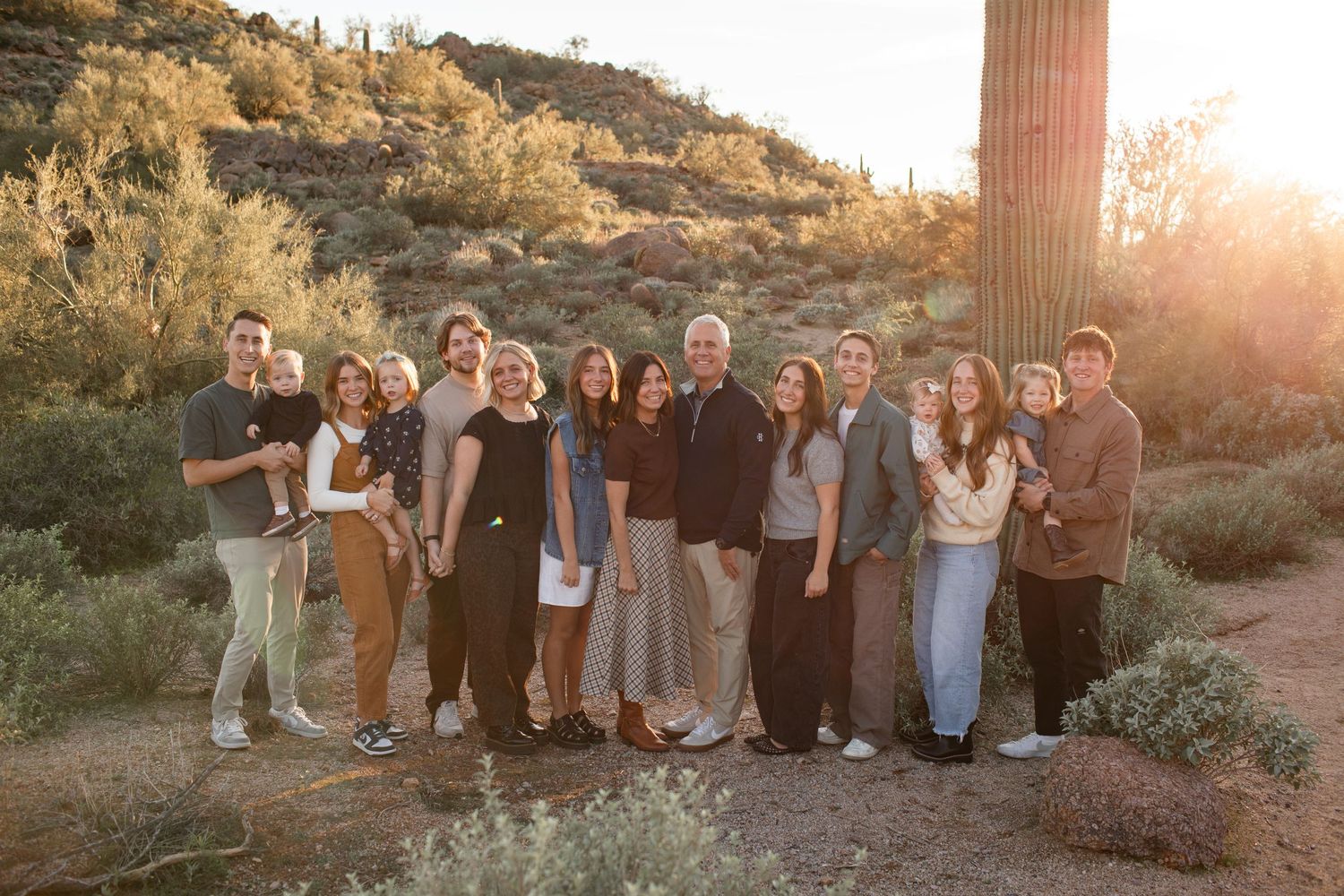 A large family group poses together at sunset in front of a desert mountain landscape on the Merkle Trail at Usery Pass in Arizona.