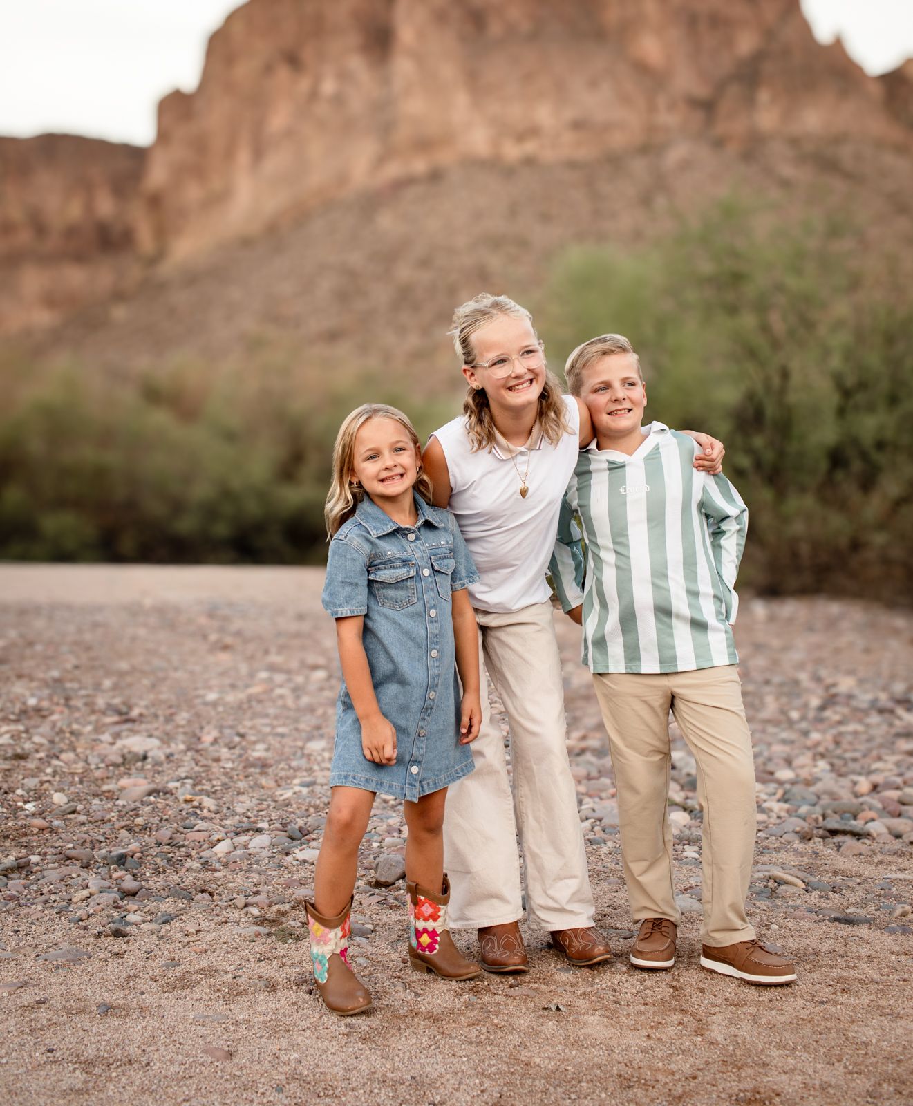 Three young people pose together on a desert trail with red rock formations in the background at sunset at Water Users recreational area.