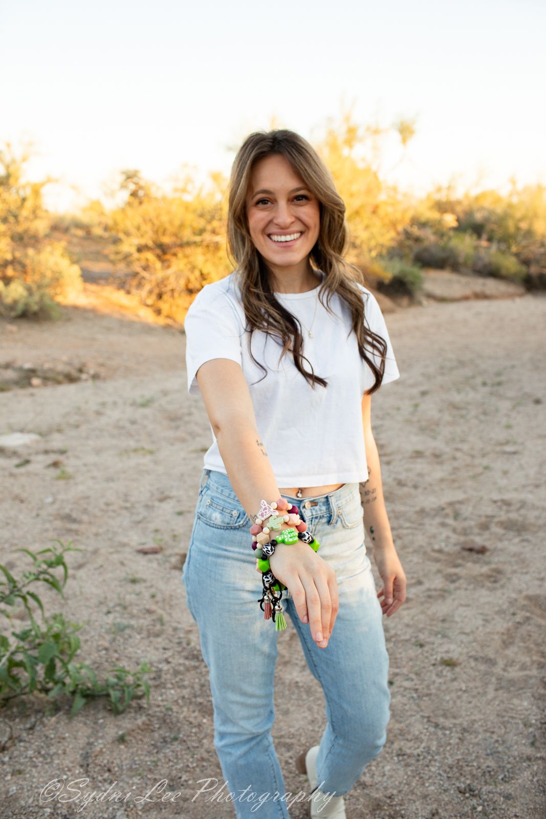 Person in casual denim and white shirt showing off colorful bracelets in desert setting.