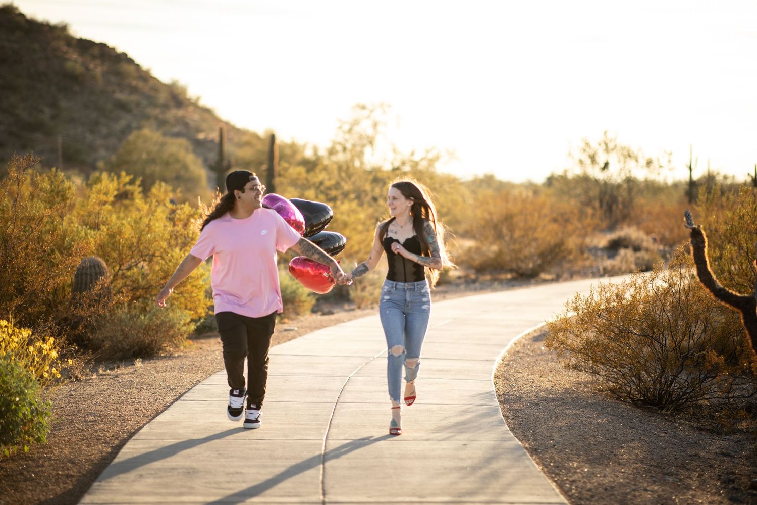 Two people run together on a desert trail at sunset with golden light illuminating the path ahead at Desert Arroyo Park in Mesa, Arizona.